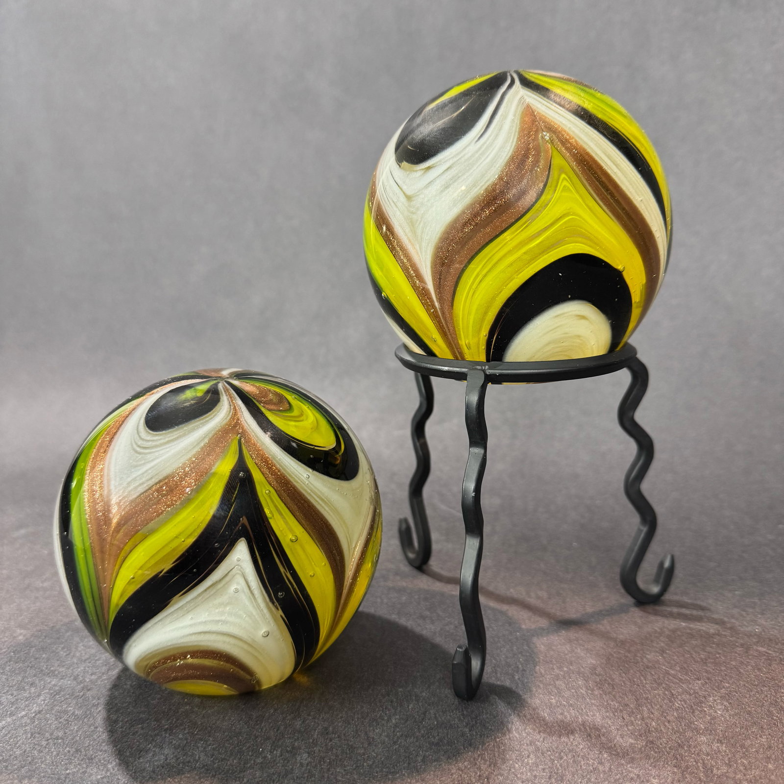 Yellow/Gold Feathers Paperweight (Set of 2 w/ Stand): Artist: Dynasty Gallery Title: Yellow/Gold Feathers Paperweight Medium: Hand-blown Glass Size: 4 H x 4 W x 4 D each Stand: 4 H x 4 W x 4 D Weight: 7 lbs. Decorative glass paperweight set that feature