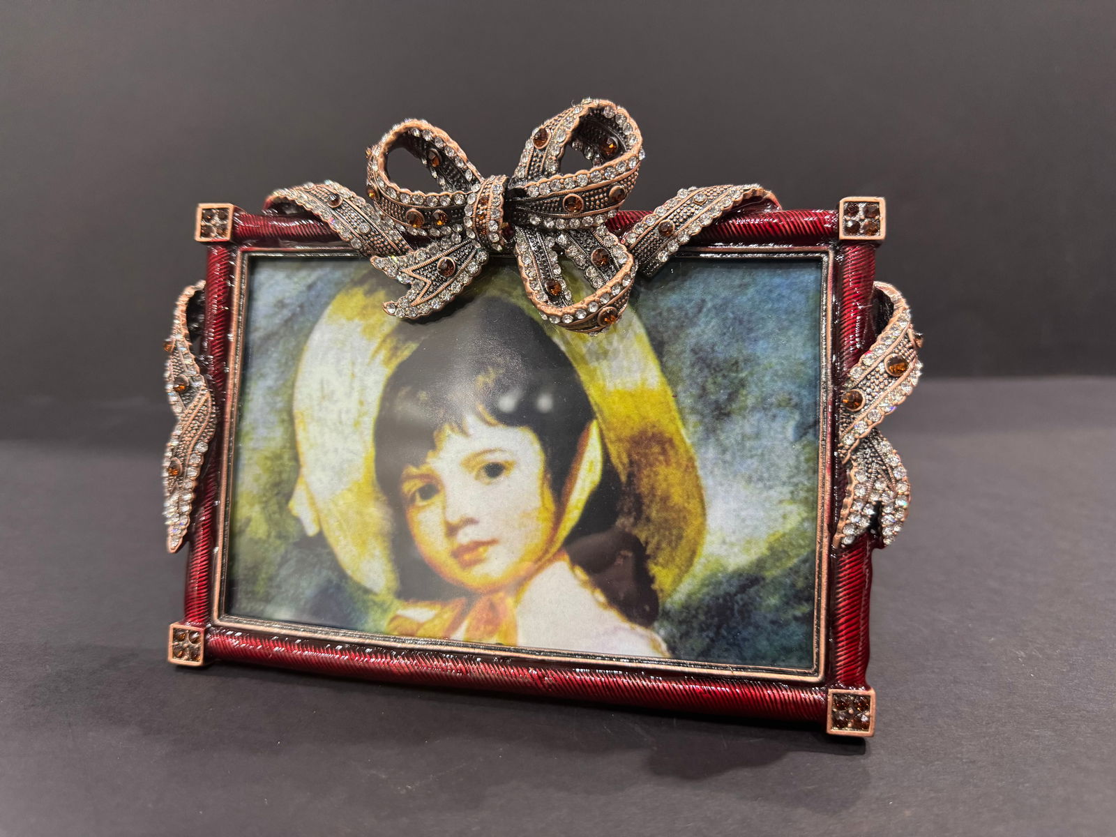 Jeweled 4x6 Bow Photo Frame: 4x6 Bow Photo Frame A decorative tabletop picture frame designed to hold a 4-6 inch photograph. The rectangular frame features a deep red, textured border with metallic corner accents. An ornate bow