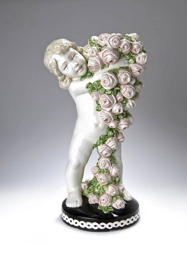 Carl Klimt, Putto mit Rosen, um 1910: Stehende Knabenfigur mit lockigem Schulterhaar, in den Armen eine üppige, bis auf den Boden reichende Girlande aus Rosenblüten haltend; runder, gewölbter Sockelstand. H. 49 cm. In Art der Jahreszei