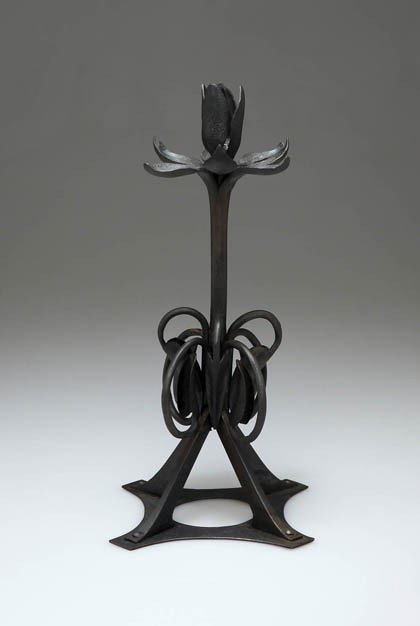 Otto Eckmann, Kerzenleuchter, 1898: Ausführung: J. Zimmermann & Co., München. Schmiedeeisen, schwarz patiniert, gelötet, genietet, Tülle in Form einer stilisierten, vierblättrigen Blüte. H. 26,3 cm.Deutsche Kunst und Dekoration, B