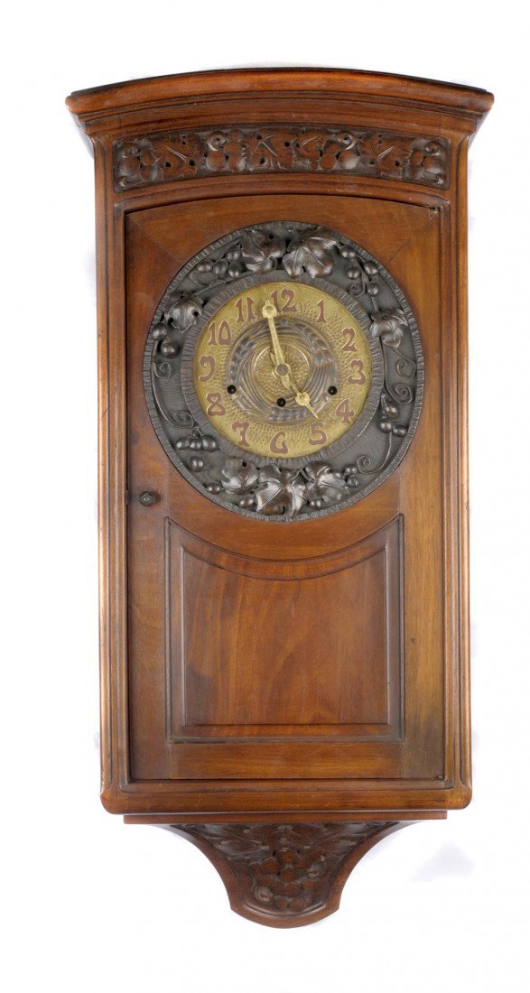 Louis Majorelle, Nancy, Wanduhr, um 1925: Eintüriges Gehäuse. Nussbaum, braun gebeizt, Schnitzdekor mit Weinlaub, Ziffernblatt aus Messing, bez.: MONNOT, NANCY (geprägt), schmiedeeiserne Montierung mit Weinlaubdekor. Uhrwerk aus Messing, m