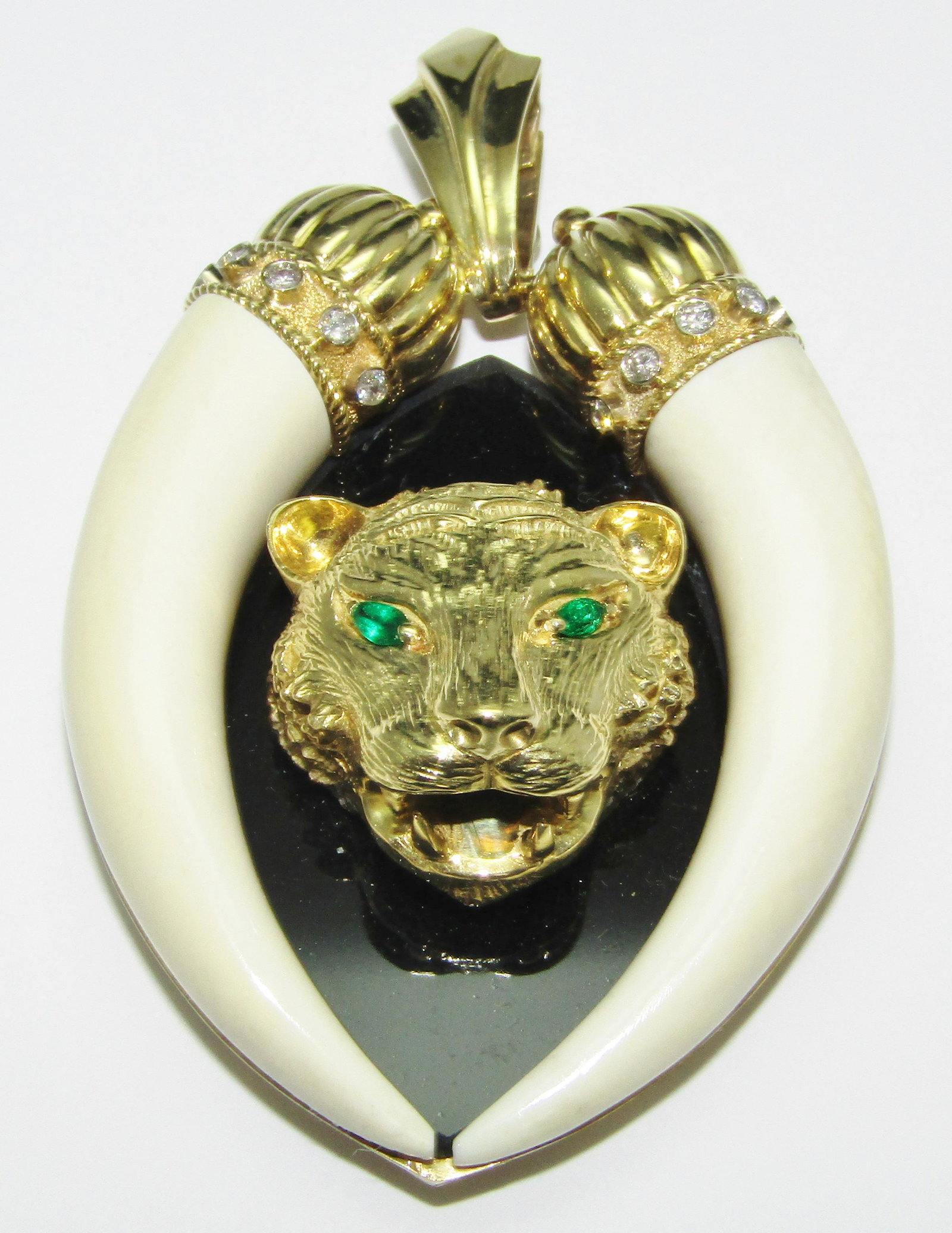 18Kt Gold Lion and Tusk Pendant with Onyx, Emeralds and Diamonds: 18 karat yellow gold lion and tusk pendant on onyx with 2 emerald eyes and has diamond melee. 75.1 grams. Measures 3" tall x 2.25" wide, and and 1" bale. Appraised Fair Market Value (FMV) is $1000.