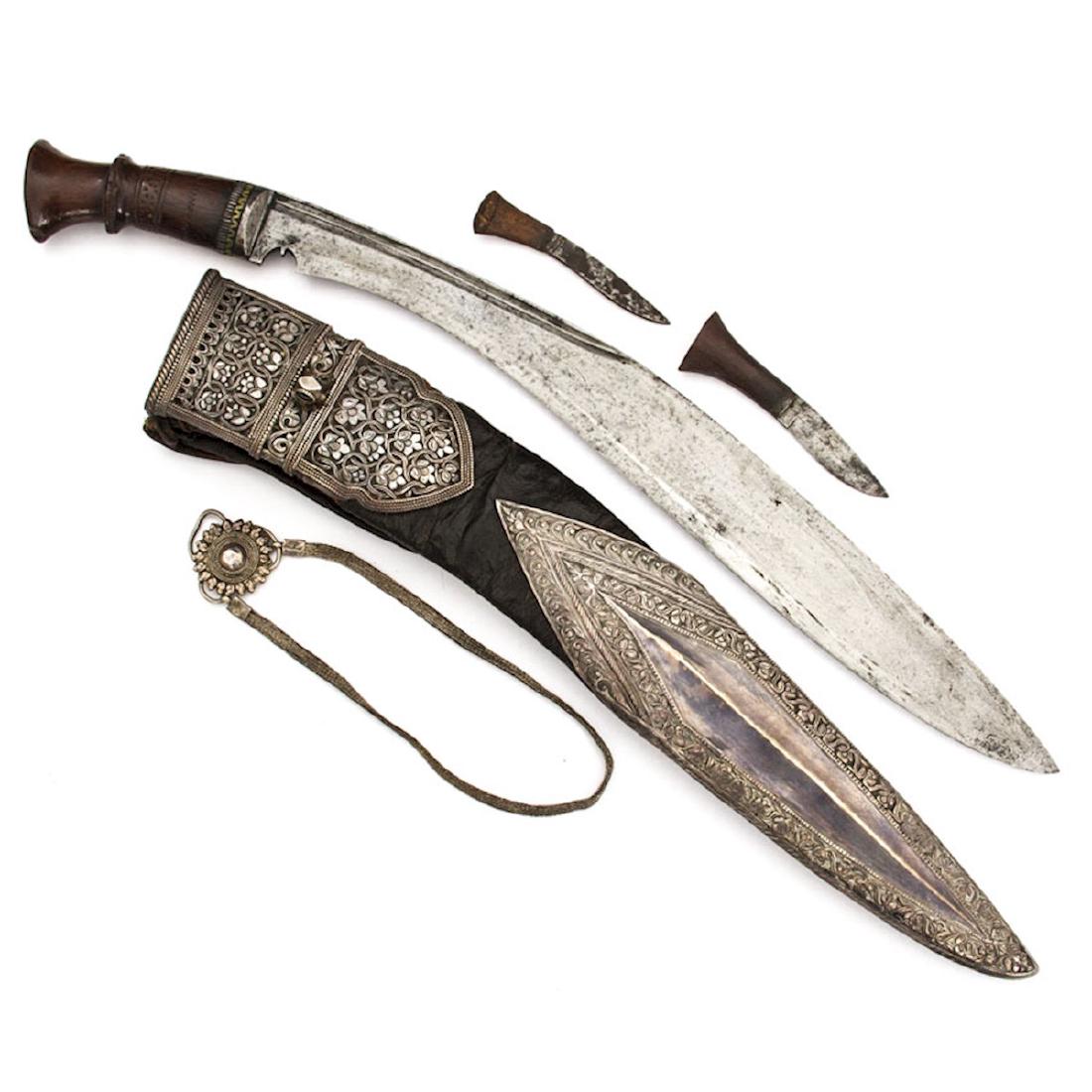 SILVER MOUNTED KUKRI KNIFE, NEPAL, 19TH C.: Scabbard is decorated with ornate silver chapes over black leather with silver straps and medallion, two utility knives with wooden grips. length 20 1/5 in.
