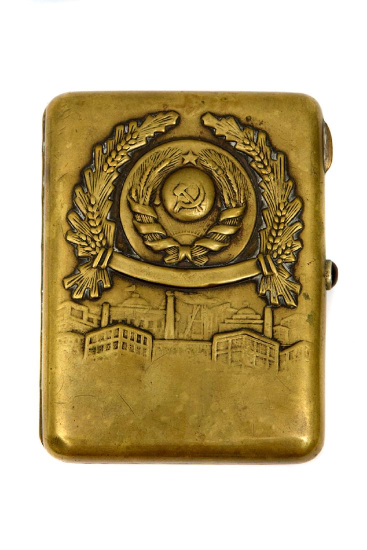 EARLY SOVIET BRASS CIGARETTE CASE WITH REPOUSSE USSR: Made of solid brass this cigarette case features the first Soviet symbol with only four Soviet republics on it, 1923. Six ribbons wrapped around the wheat represent the six languages officially spoken