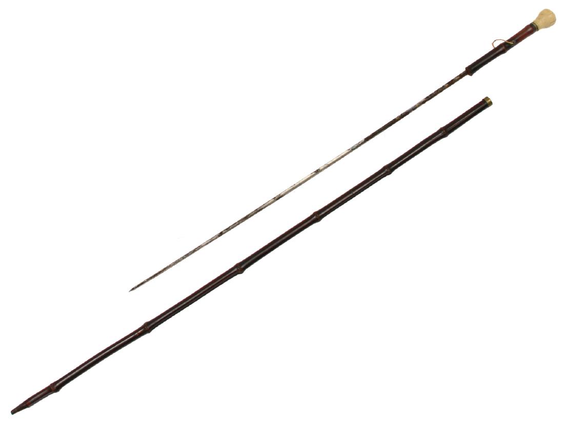 CANE WITH CONCEALED BLADE SWORD, 19TH C.: A cane (probably French) with ball-shaped carved handle, hidden stiletto-type triangular shape blade decorated with bluing and gilt, wooden shaft. Dimensions: L: 33 in., (83.8 cm.)