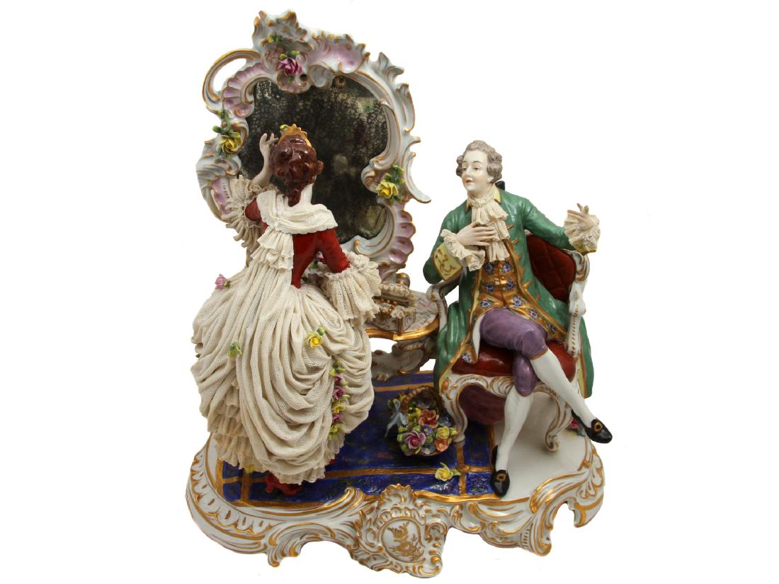A RUDOLSTADT PORCELAIN FIGURAL GROUPING, 19TH C.: A Rudolstadt Volkstedt hand painted gilt porcelain figural grouping consisting of a woman in extravagant lace dress looking into the mirror and man admiring her from aside. Blue glaze mark behind the 
