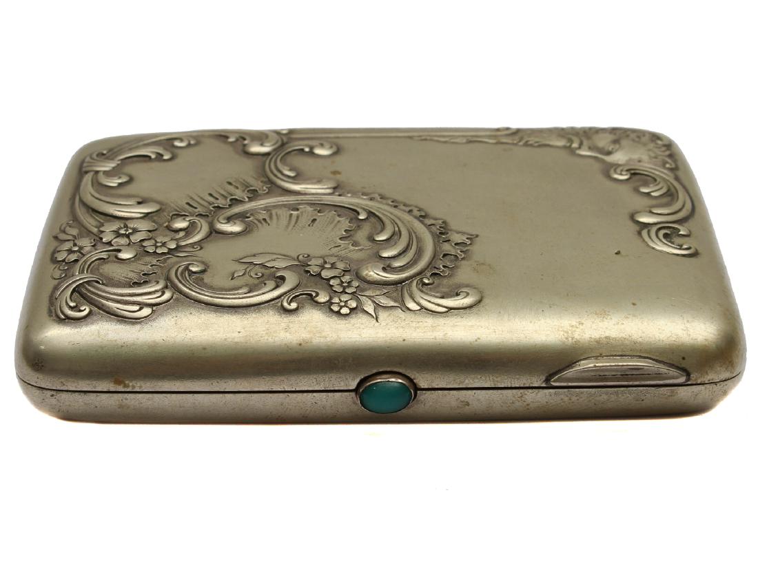 A RUSSIAN IMPERIAL SILVER GILT GEM CIGARETTE CASE: A Russian parcel gilt silver cigarette holder featuring a high relief depicting a mythological god looking down on wind swirls and flowers. Silver hallmarks on the interior: two Cyrillic letters: "G.S