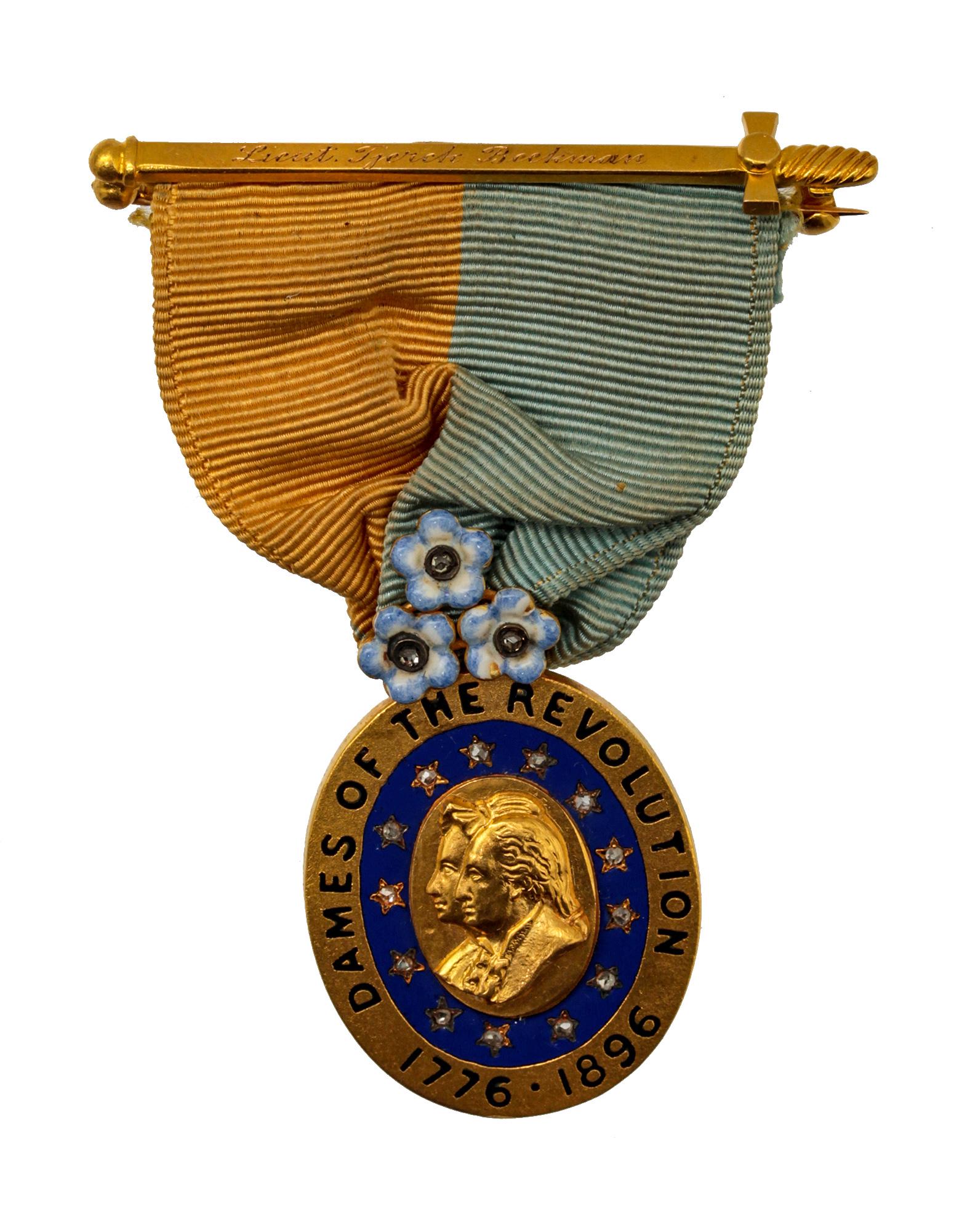 AN ANTIQUE 18K GOLD MEDAL DAMES OF THE REVOLUTION: An antique American late 19th-century medal. The medal is constructed of a blue oval in the center with a gold oval with a relief depicting a man and woman in profile. On a blue background, there are 