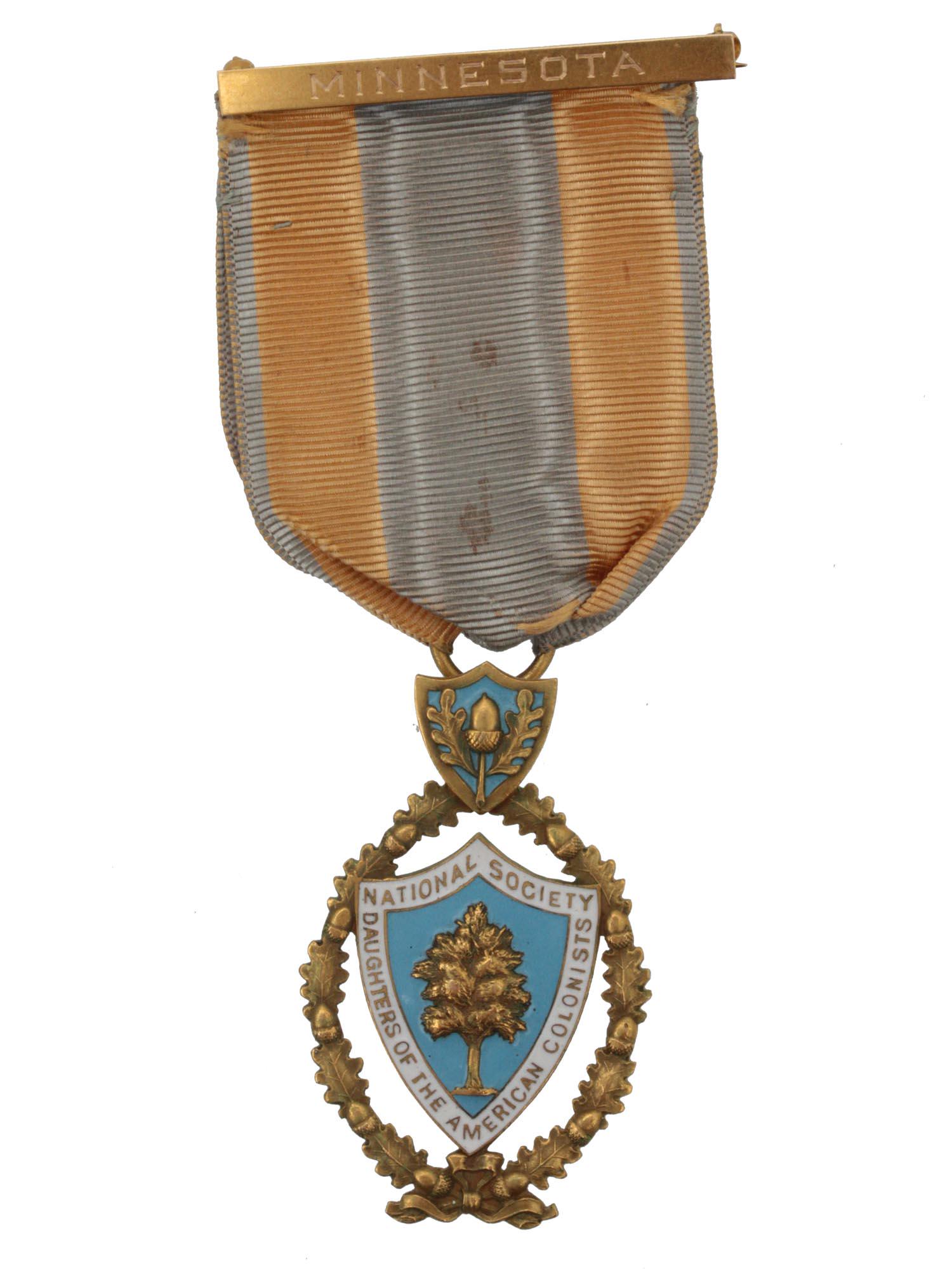 A DAUGHTER AMERICAN 14K GOLD COLONIST MEDAL: A 14k gold National Society Daughters of the American Colonist (D.A.R) medal with a Minnesota ribbon. The obverse is marked with a reward to Della G. Webb. S/N 566. The medal is manufactured by JEC &