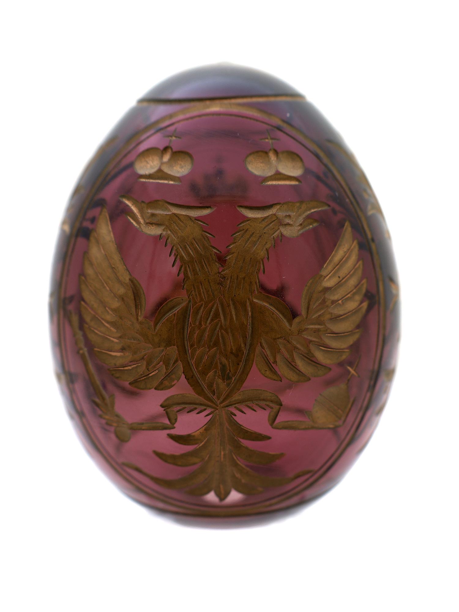 A RUSSIAN IMPERIAL ETCHED GLASS EASTER EGG: Russian Easter egg made of amethyst glass. The handblown glass egg is engraved and gilded on one side with a double-headed eagle with scepter and orb held in its talons, the opposite side with the cro