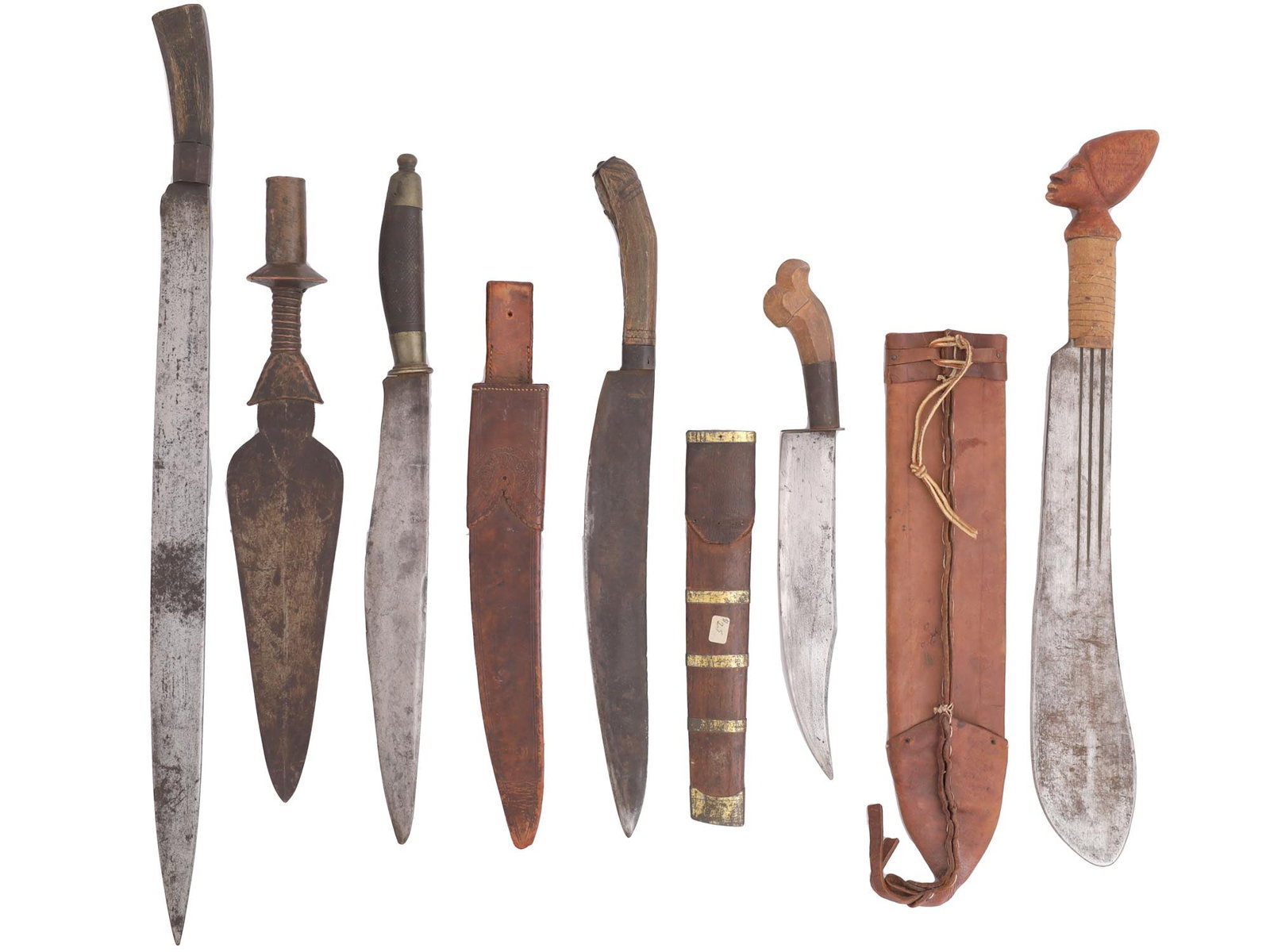 A SET OF FIVE BLADED WEAPONS OF VARYING TYPE AND ONE SPEAR HEAD: A set of five bladed weapons and one spear head. Some of the weapons appear to be of Caribbean origin. The machete type weapon with a head sculpture on the pommel bears the inscription 'Trinidad' on i