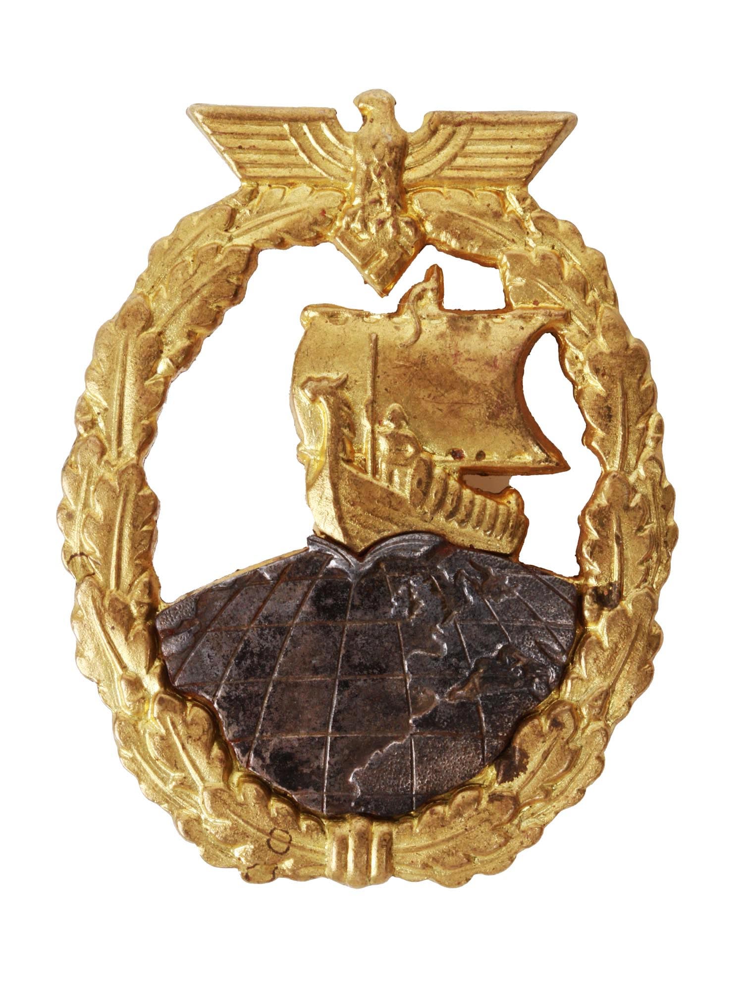 A NAZI GERMAN WW2 KRIEGSMARINE AUXILIARY CRUISER BADGE: A Nazi Germany WW2 Kriegsmarine Auxiliary Cruiser war badge produced in zinc. Designed as a Viking longship sailing boat over the northern hemisphere of the globe surrounded by a laurel wreath of oak 