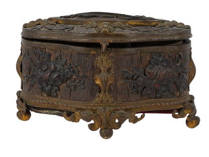 A FRENCH NAPOLEON III GILT BRONZE AND CARVED WOOD JEWELRY CASKET, C. 1860–1880: A highly ornate Napoleon III-era French jewelry casket, combining gilt bronze mounts with elaborately carved dark-stained wood panels, most likely walnut or oak. The box rests on four scroll-footed or