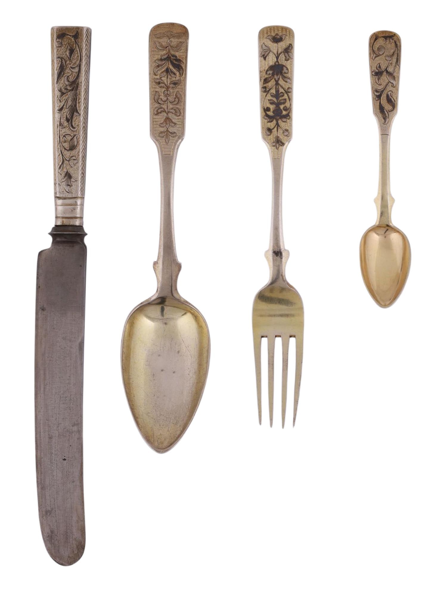 A RUSSIAN GILT-SILVER AND NIELO FLATWARE SET, 19TH CENTURY: Comprising a knife, fork, tablespoon, and teaspoon, each with engraved and niello-decorated handles of floral design in the Neo-Russian taste. The gilt bowls and tines retain much of their original fi