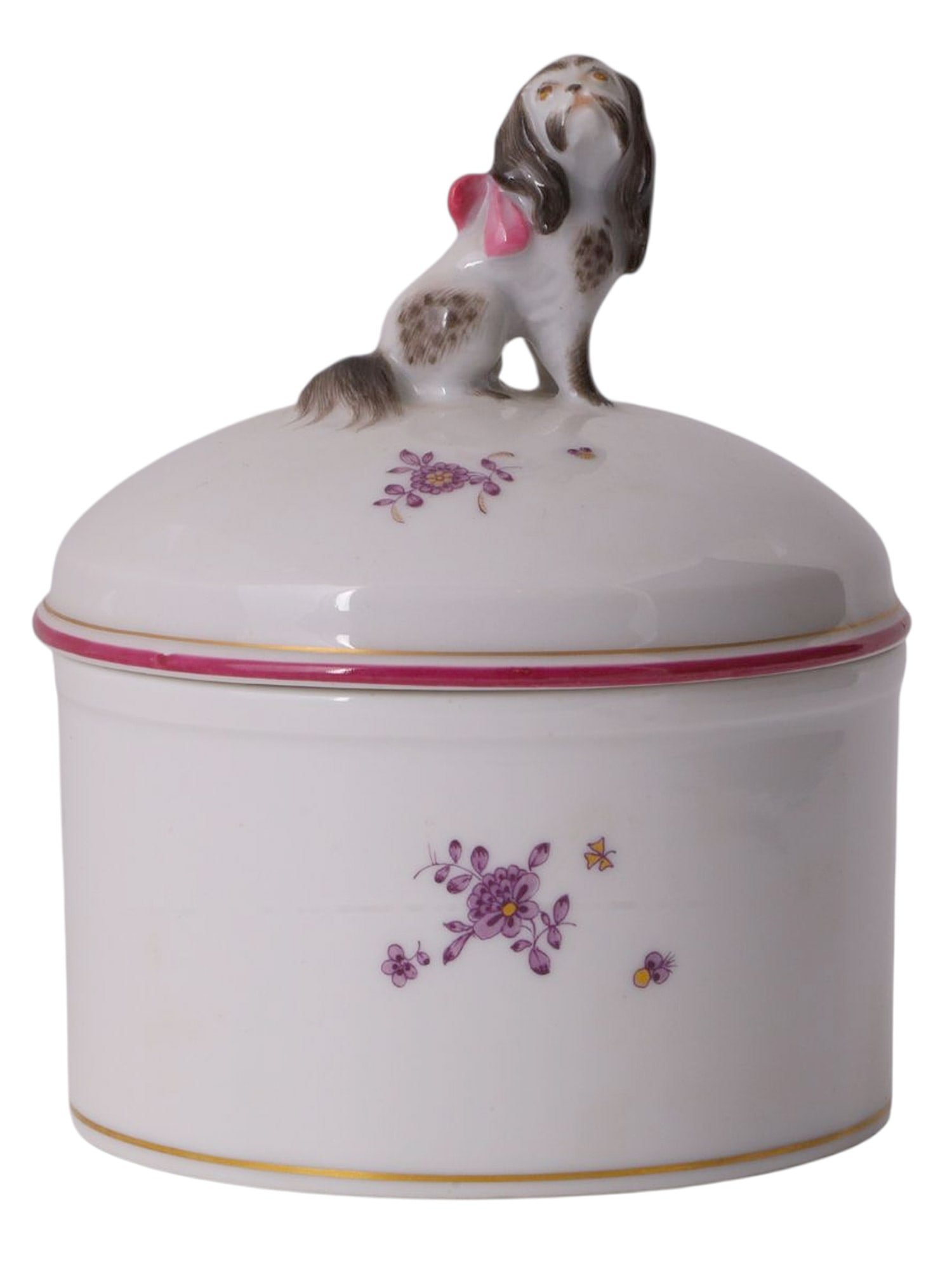A MEISSEN PORCELAIN LIDDED CONTAINER WITH A DOG FINIAL, C. 1937-1945: Hard-paste porcelain of cylindrical form, the domed lid surmounted by a finely modeled seated lapdog with long ears and tail, painted in naturalistic tones and wearing a pink ribbon bow. The box and c