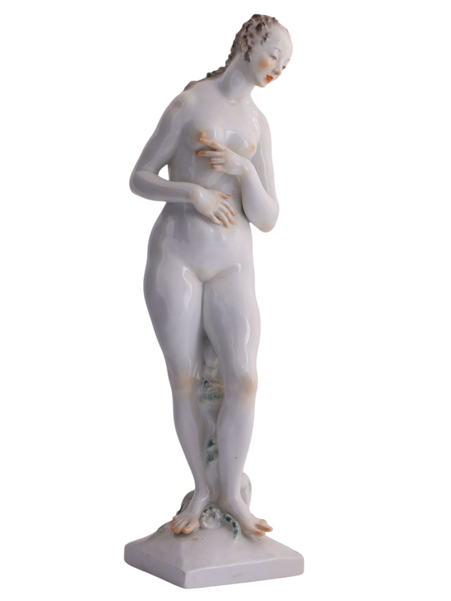 A PAINTED PORCELAIN FIGURE OF A NUDE LADY: White porcelain figure modeled as a standing nude "Venus" in a contrapposto pose, with the head gently inclined and the arms drawn inward in a modest classical gesture. The sculptural treatment is ref
