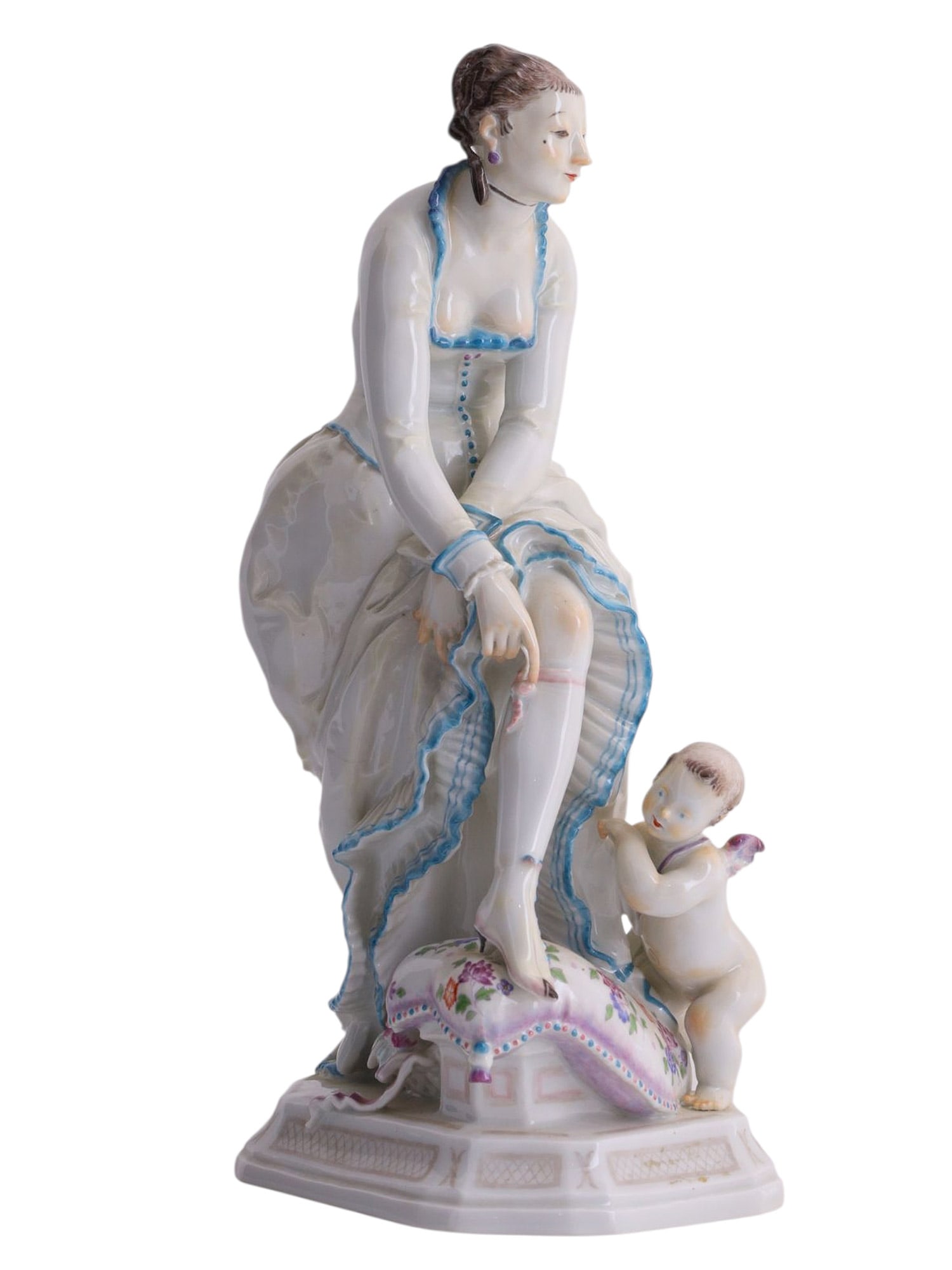 A MEISSEN PORCELAIN FIGURAL GROUP "DAME MIT AMOR" BY PAUL SCHEURICH, C. 1923: Modeled as an elegant seated lady lifting her skirt to reveal a stockinged leg, accompanied by a small winged Amor climbing beside her and leaning against a richly decorated cushion, the composition i