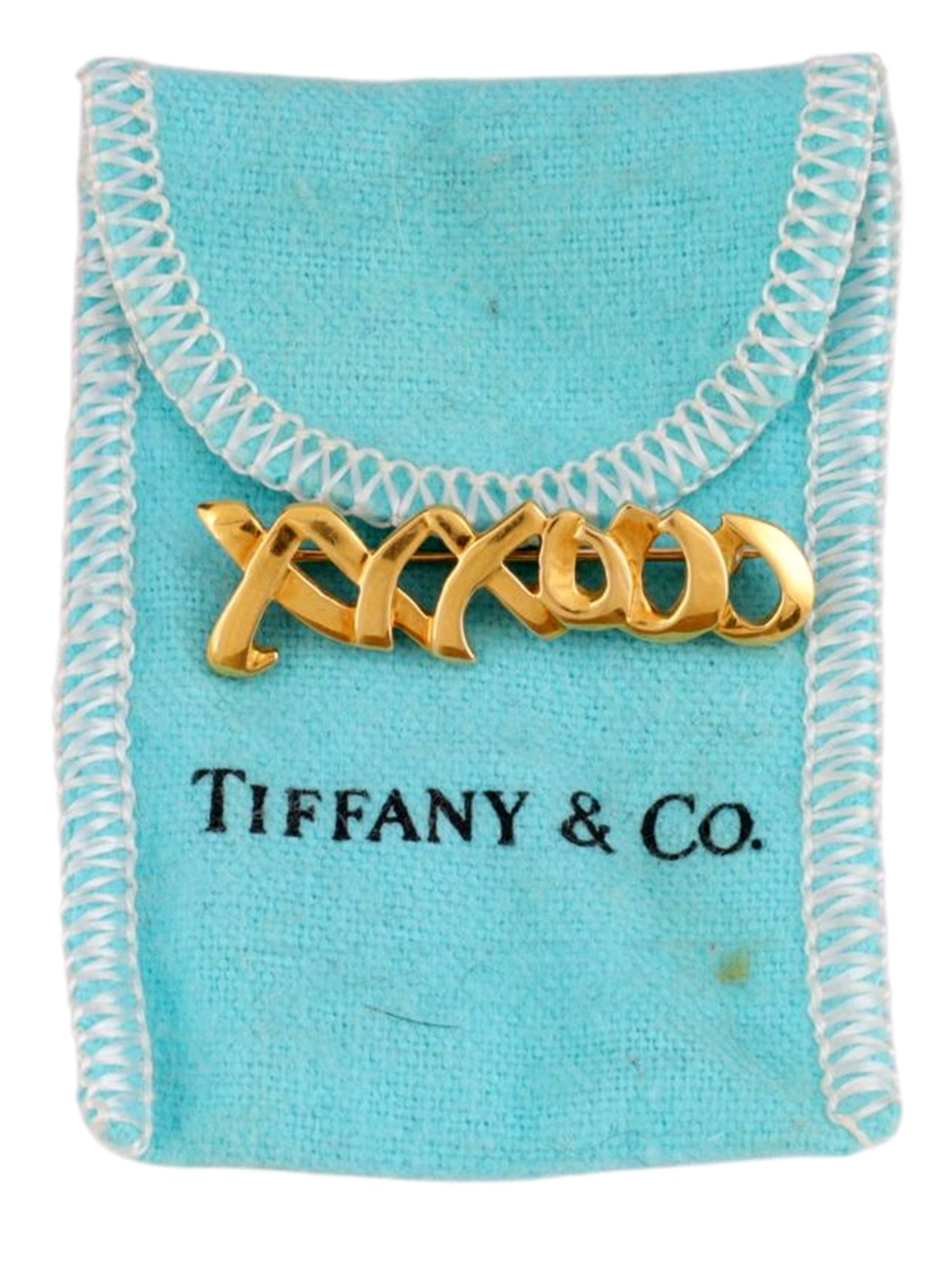 AN AMERICAN GOLD CALLIGRAPHIC BROOCH, TIFFANY & CO., DATED 1983: Cast and polished yellow gold brooch formed as a continuous sculptural calligraphic inscription executed in openwork, the fluid interlaced letterforms modeled in a bold modernist interpretation of orn