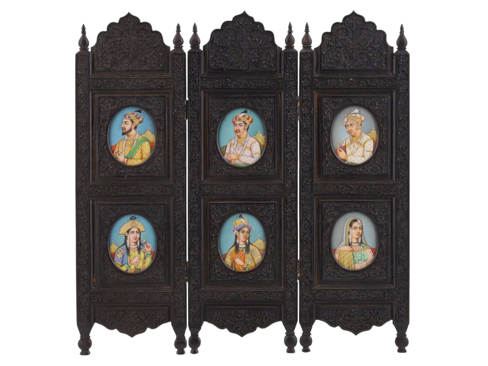 A MINIATURE INDO-PERSIAN PRIVACY SCREEN WITH SIX PORTRAITS: The screen is constructed of three hinged vertical panels in dark, densely carved hardwood, each surmounted by a scalloped arch crest with finials and supported on turned feet. Each panel is fitted wi