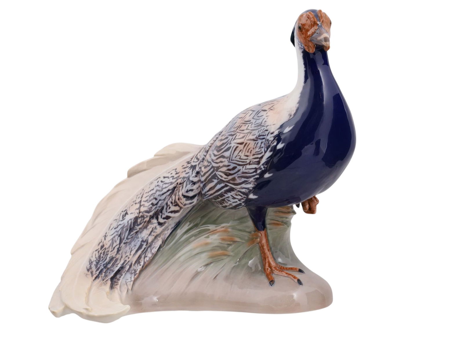 A COPENHAGEN PORCELAIN FIGURE OF A PEACOCK, BING & GRONDAHL, DENMARK, 20TH C.: Naturalistically modeled standing on a grassy mound, the bird with a cobalt-blue breast and finely painted plumage in shades of grey, cream, and black, the tail swept to one side. Underglaze factory m