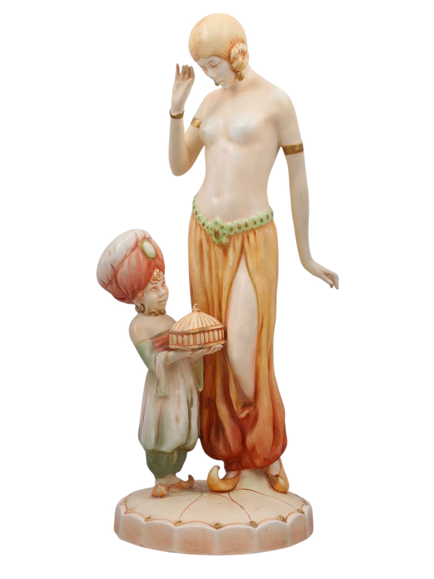 A ROYAL DUX STYLE CZECHOSLOVAKIAN POTTERY FIGURE, EARLY 20TH CENTURY: Depicting a partially draped Orientalist maiden with gilt armbands and flowing trousers, accompanied by a young page or attendant in a turban holding a domed tray. The figures stand upon a scalloped b