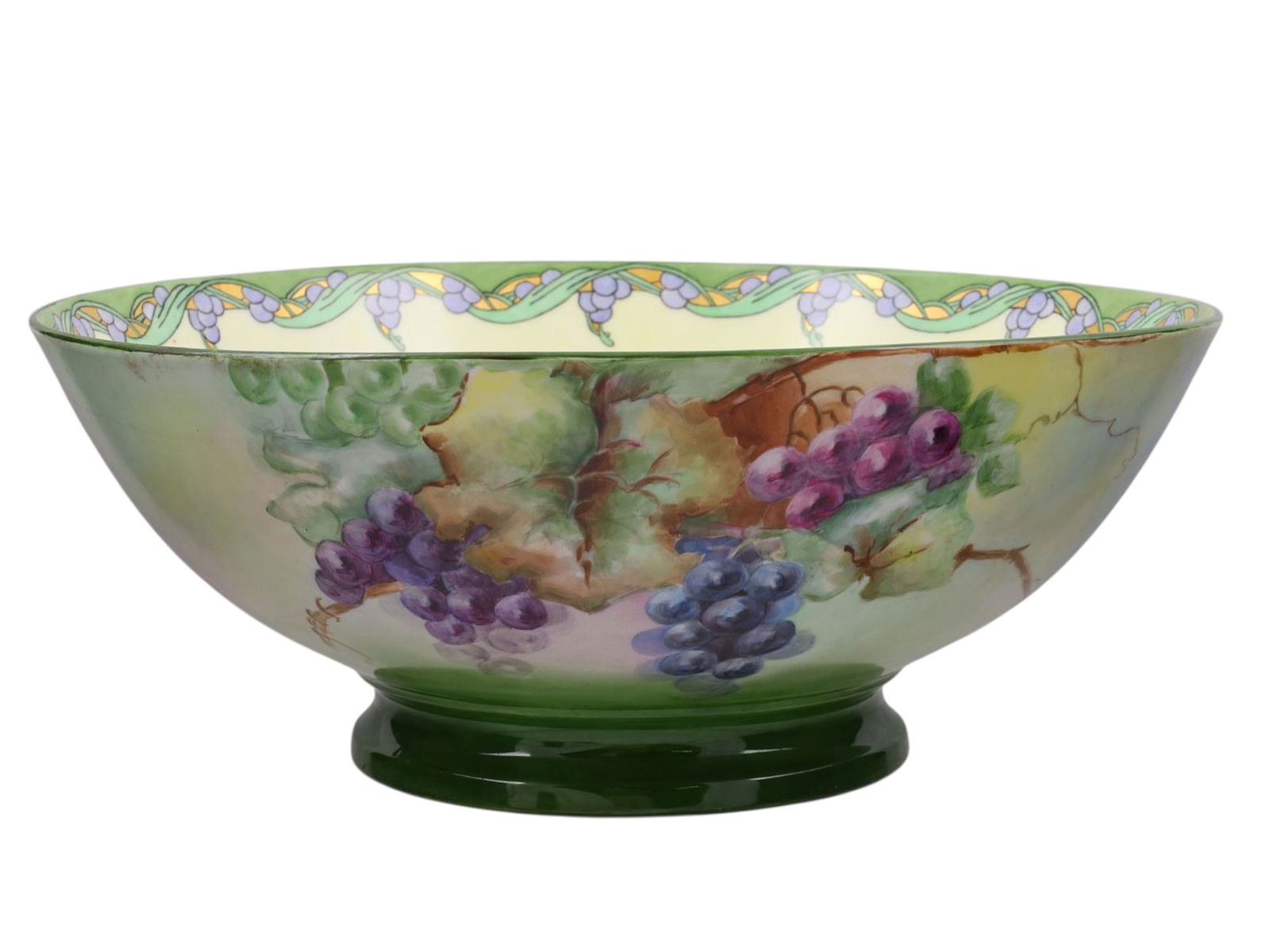 A LIMOGES PORCELAIN PUNCH BOWL, D&C FRANCE, EARLY 20TH CENTURY: Of large circular form on a raised foot, the exterior is finely hand-painted with abundant grape clusters in tones of green, purple, red, and violet amidst foliage against a soft green and cream groun