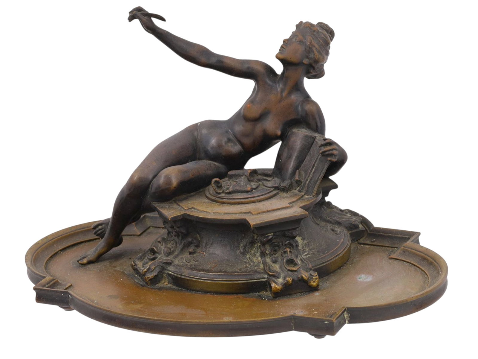 A BRONZE FIGURAL INKWELL, NUDE WOMAN WITH A BOOK AND PEN, FRANCE, 19TH CENTURY: A finely cast patinated bronze figural inkwell depicting a seated nude female allegorical figure, leaning gracefully against an open book while extending one arm upward holding a pen. The figure rests