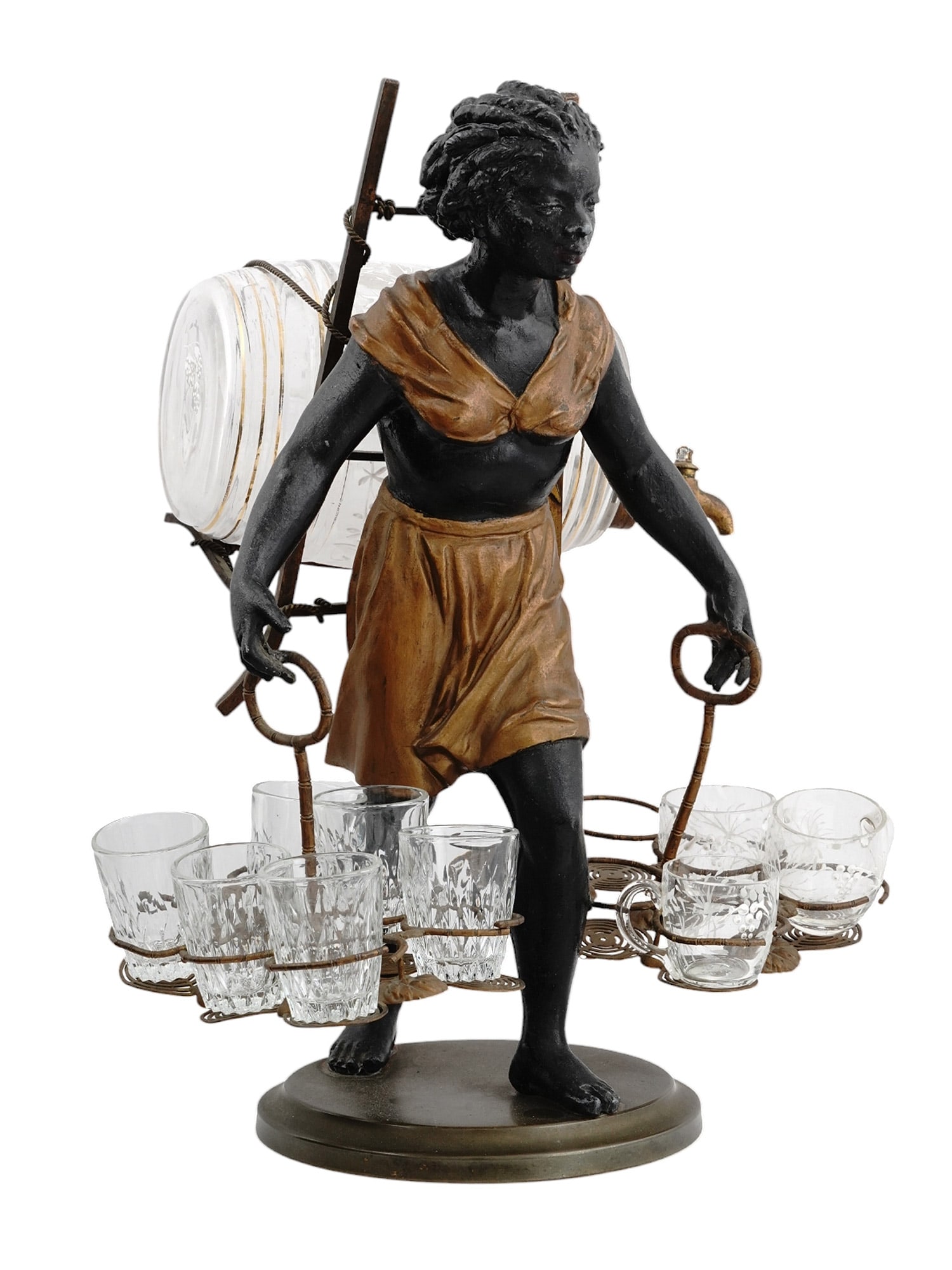A PAINTED METAL MOORISH FIGURE WITH A GLASS DECANTER & CUPS: A liqueur cellar in polychrome spelter, made in the shape of a young boy carrying a glass barrel and nine glasses. The barrel is decorated with beautiful etched berries and leaves. Dimensions: H: 13 3