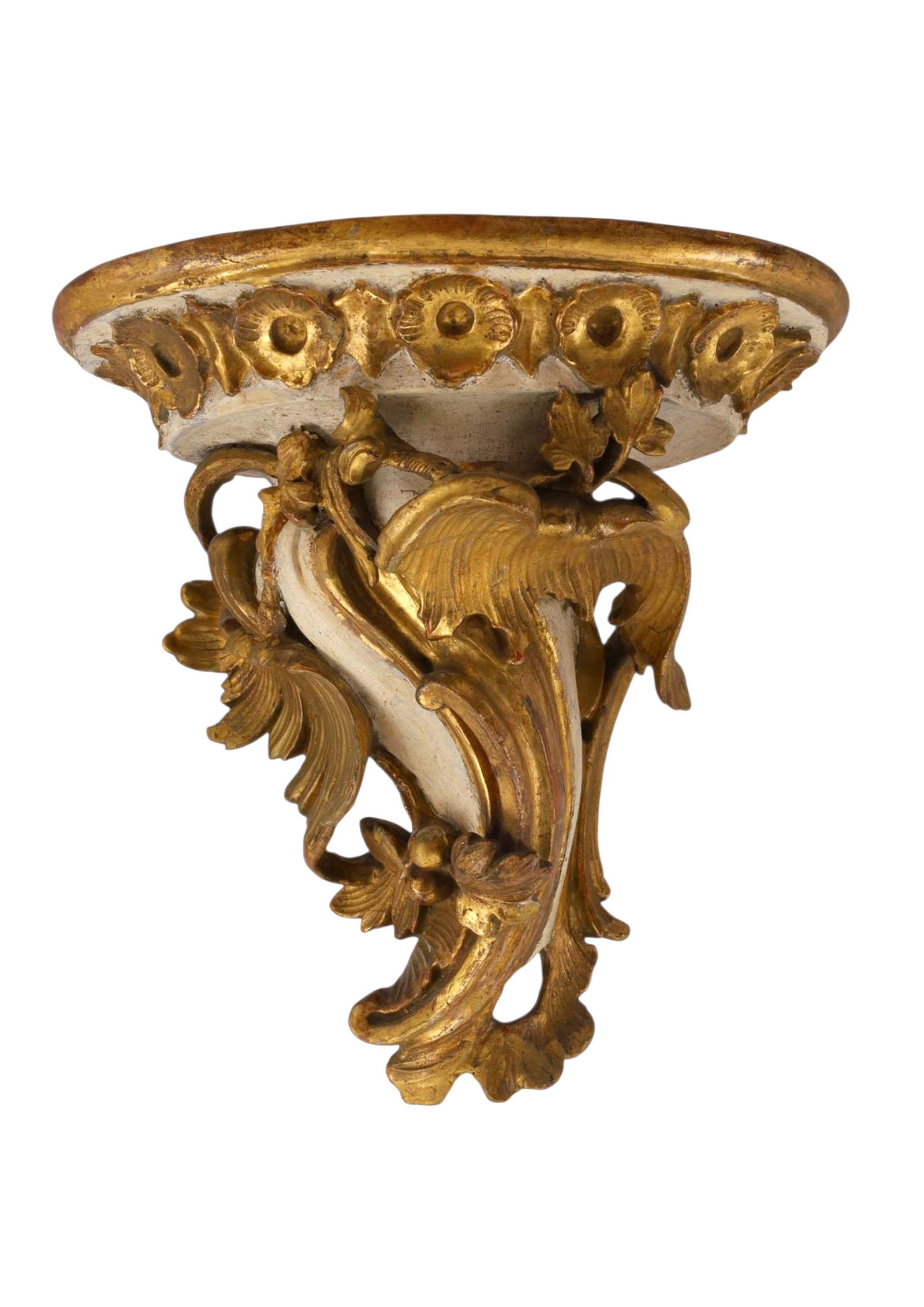 AN ITALIAN GILTWOOD WALL BRACKET, 18TH CENTURY: Of carved and gilded wood in Italianate Rococo style, the demi-lune top with molded edge above a profusely carved scrolling foliate and floral support terminating in acanthus leaves. The surface retai
