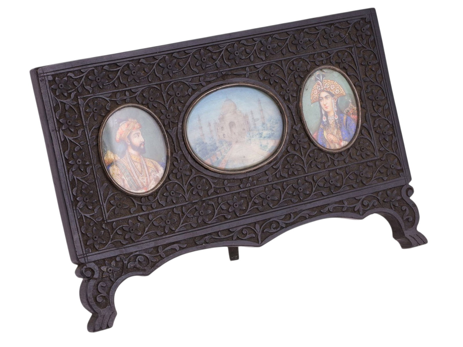 AN INDIAN CARVED WOOD TABLE SCREEN WITH MINIATURE PAINTINGS, PROBABLY RAJASTHAN OR AGRA, LATE 19TH: Of rectangular form, the screen intricately carved in dark-stained hardwood with dense foliate and floral arabesques arranged in horizontal registers, raised on shaped feet and fitted at the reverse w