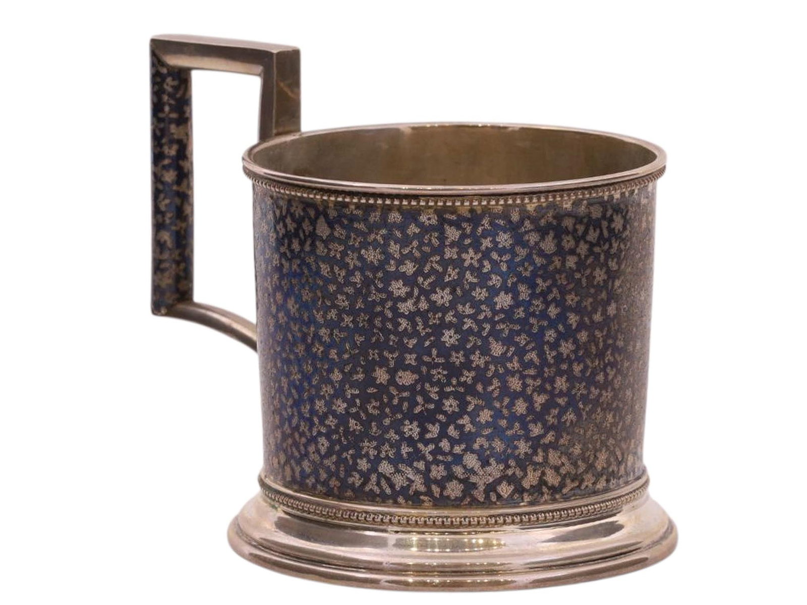 A RUSSIAN SILVER AND NIELLO TEA GLASS HOLDER, IVAN GRISHIN WORKSHOP, 1890: A cylindrical tea glass holder with a rectangular handle, decorated with a floral geometric pattern using the silver-blackening technique of niello.The bottom bears the hallmarks: "A.A. 1890" [Unknown