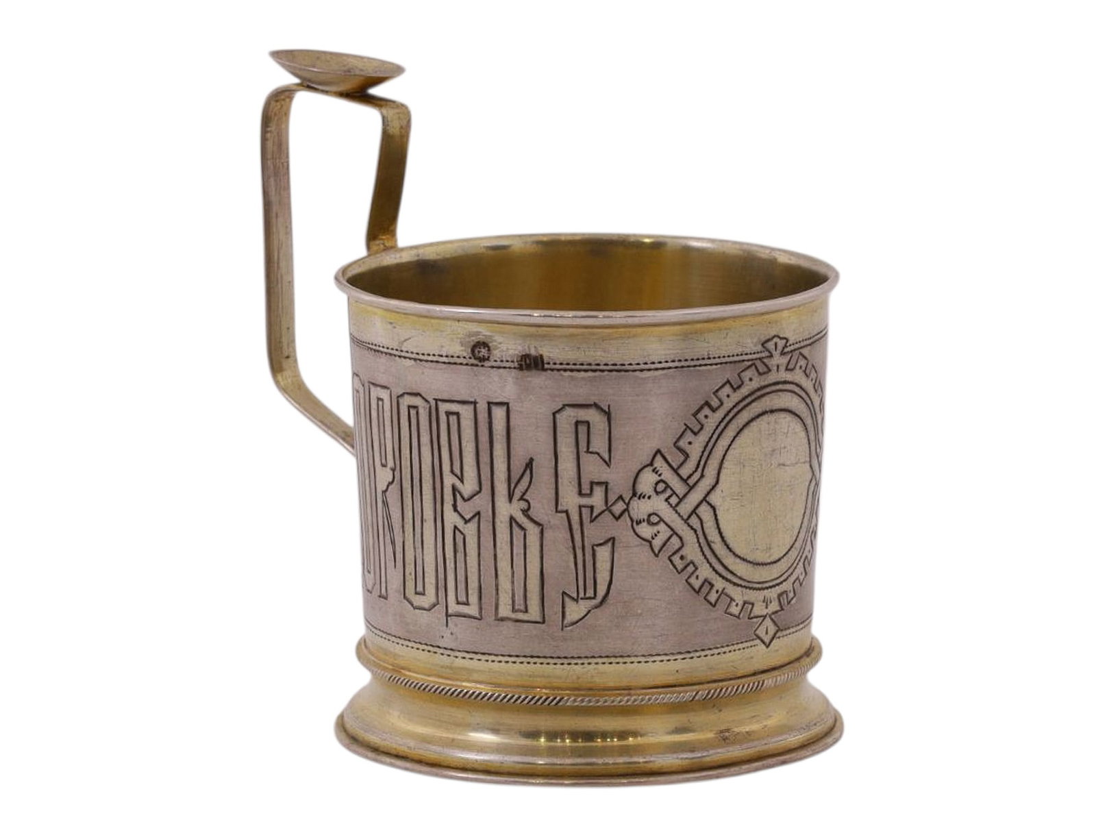 A RUSSIAN SILVER TEAGLASS HOLDER IN NEO-RUSSIAN STYLE, WORKSHOP OF NIKOLAI PAVLOV, 1889: A cylindrical tea glass holder with a rectangular handle, featuring a central ornamental engraved medallion in the Neo-Russian style and the inscription “PEYTE NA ZDOROVYE” (Drink to Your 