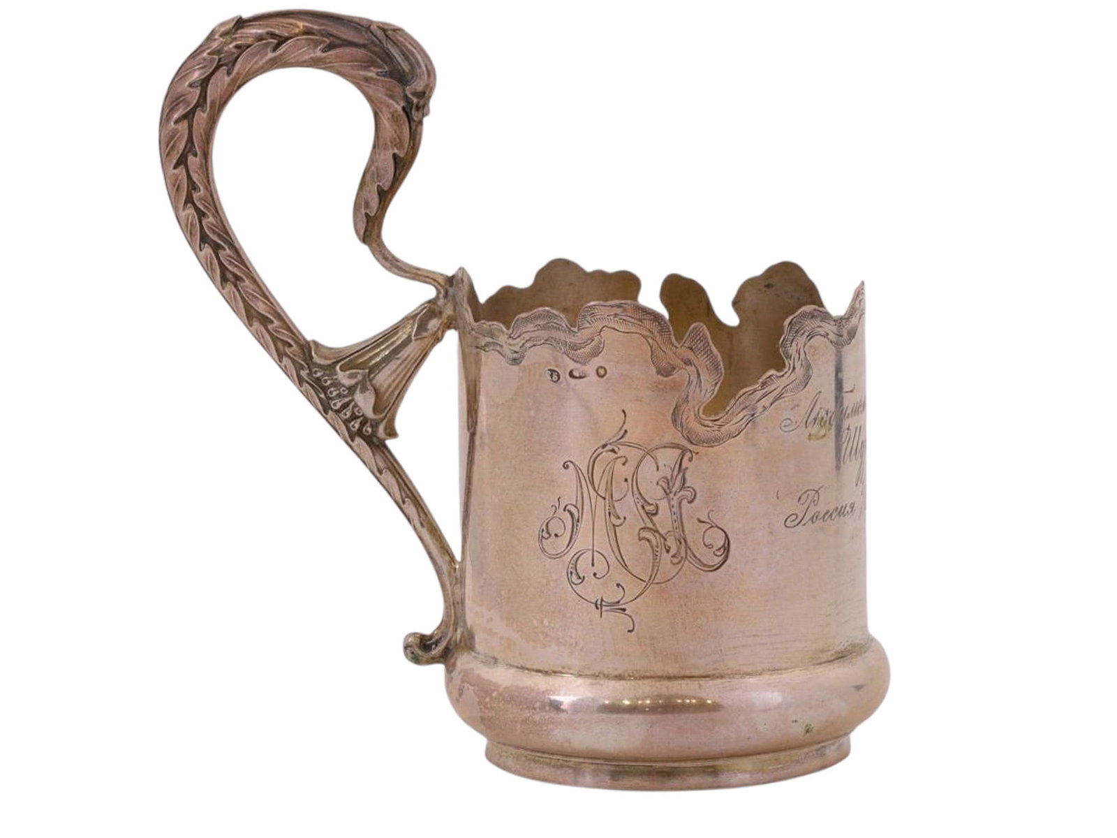 A RUSSIAN COMMEMORATIVE SILVER TEA GLASS HOLDER, VARVARA BALADANOVA FACTORY: A cylindrical tea glass holder with a handle in the Neoclassical style, featuring a leaf motif, is decorated with an asymmetrical engraved pattern; one side bears an engraved monogram, while the other