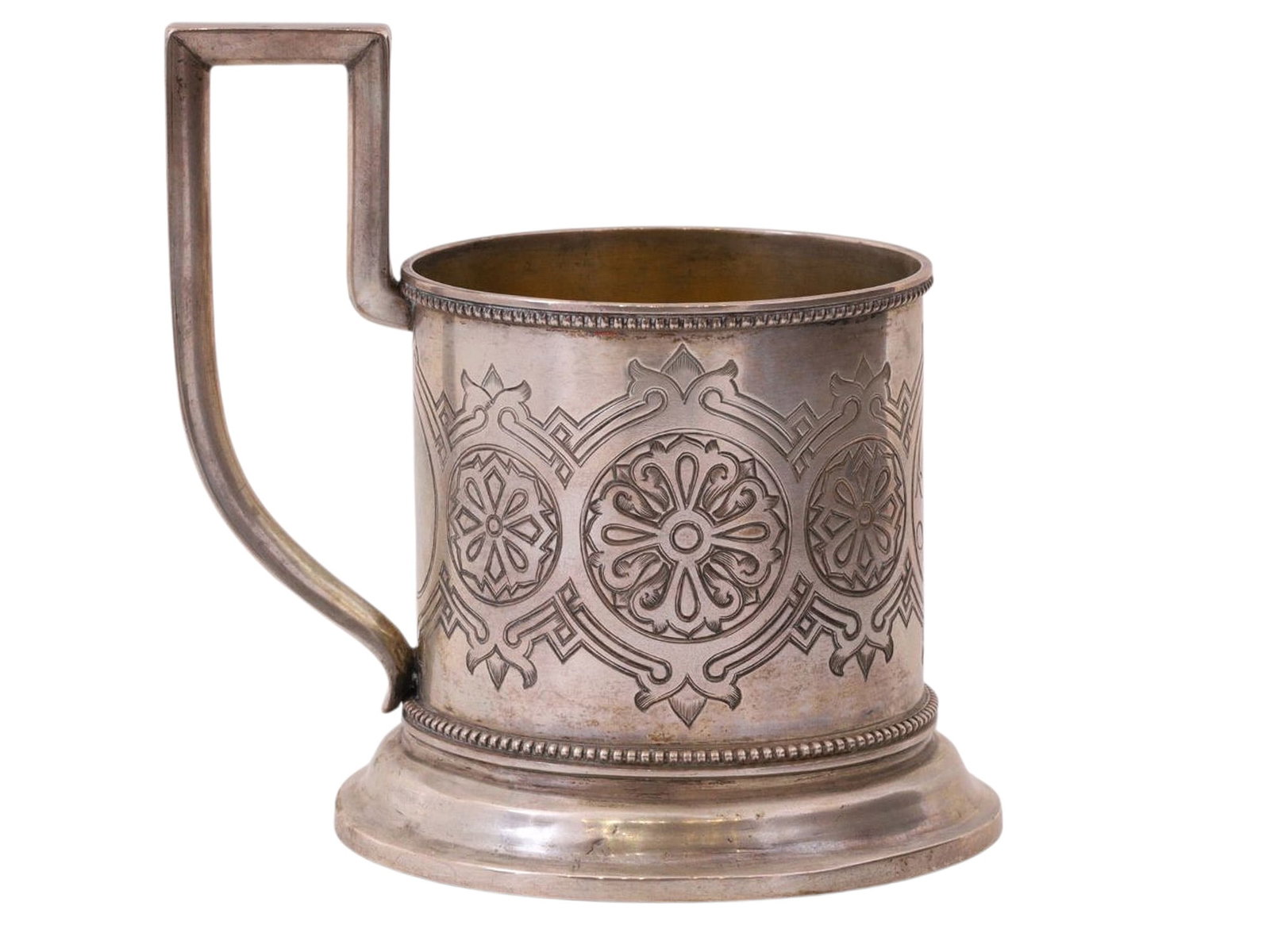 A RUSSIAN SILVER TEAGLASS HOLDER IN PAN-SLAVIC STYLE: A Russian silver podstakannik (tea glass holder) which has been delicately rendered in the pan-slavic style, showing overlapping circular and geometric forms around the body of the piece. A monogram c