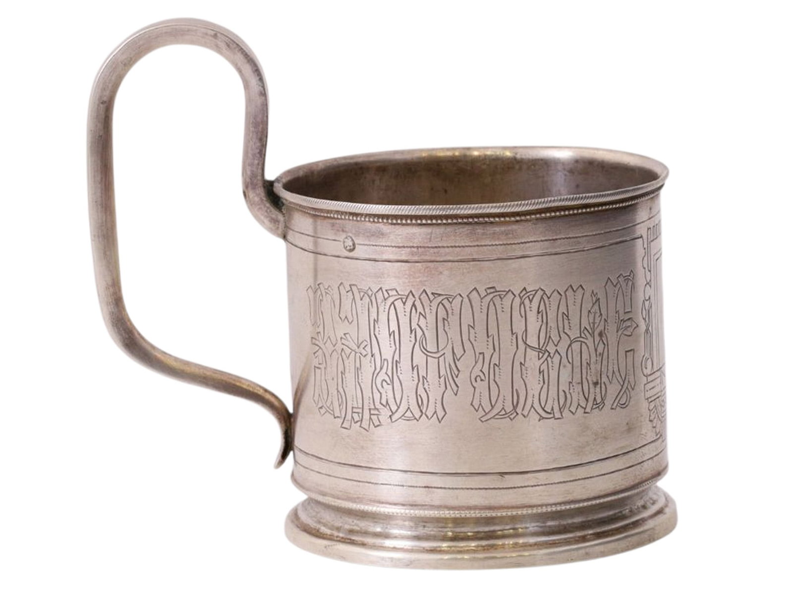 A RUSSIAN SILVER TEA GLASS HOLDER, MOSCOW, 1890: A cylindrical tea glass holder with a rounded handle, featuring a central ornamental engraved medallion in the Neo-Russian style and the inscription “DRINK TO YOUR HEALTH” around the perim