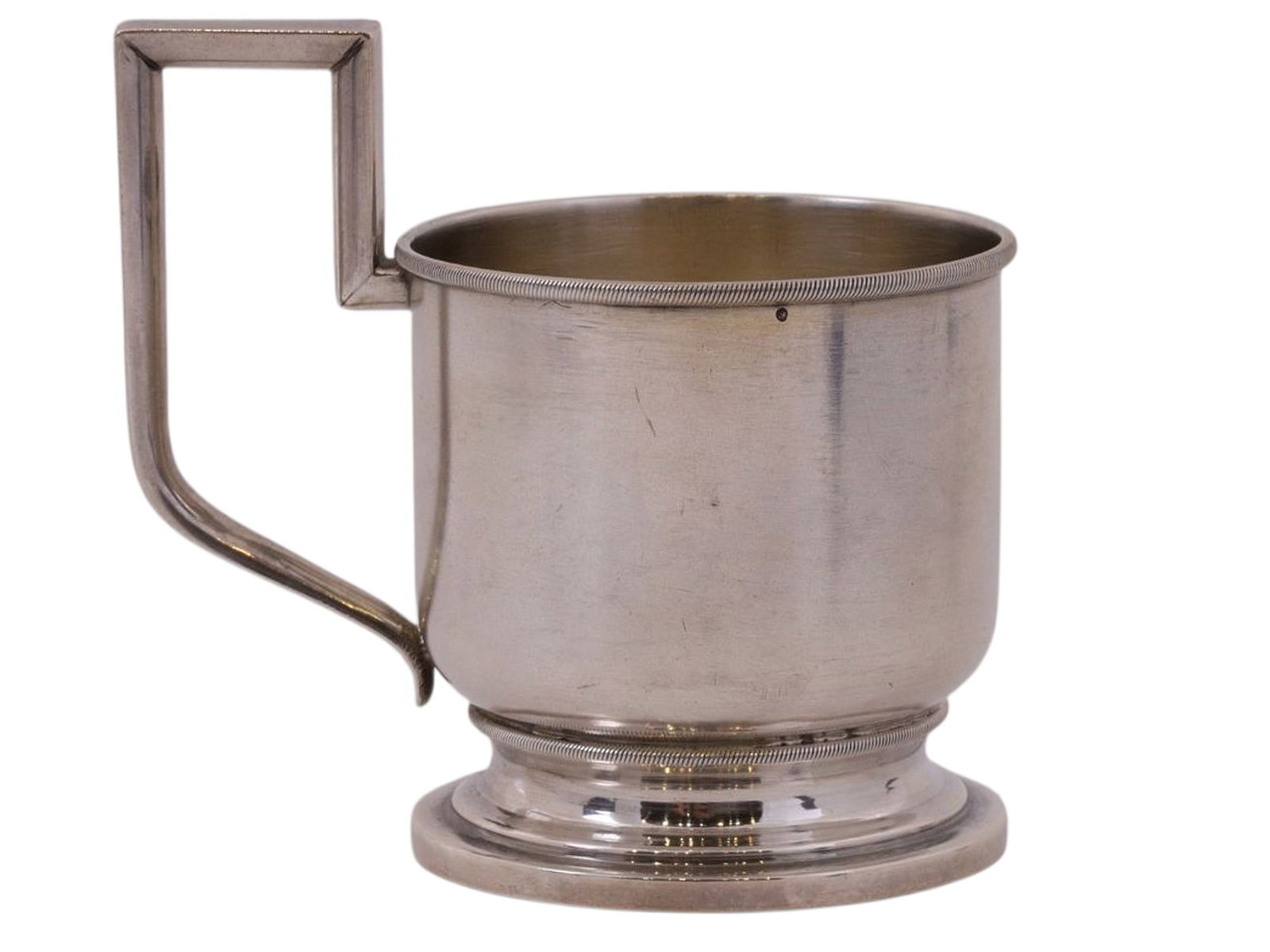 A RUSSIAN SILVER TEA GLASS HOLDER, ALEXANDER LOKIN WORKSHOP, C. 1890S: A cylindrical tea glass holder with a handle in the Neoclassical style, featuring a simple decorative motif of narrow grooves along the upper and lower rims.The body and base of the coaster bear the f