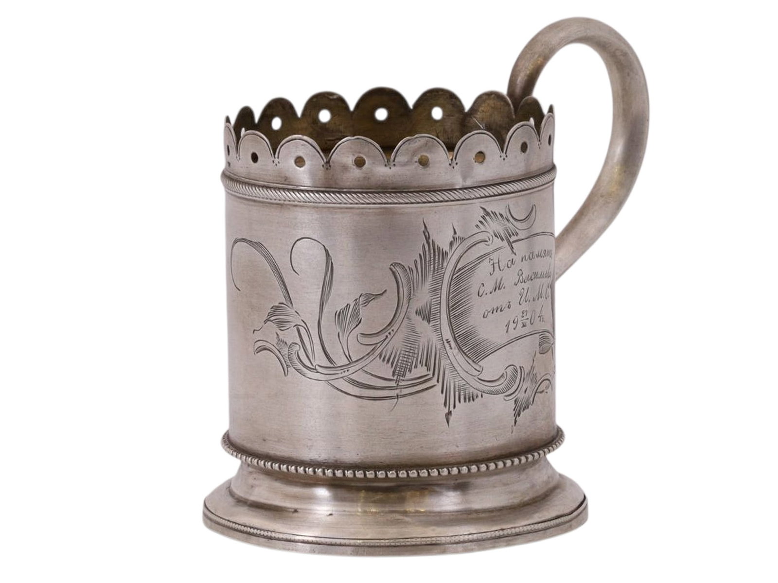 A RUSSIAN COMMEMORATIVE SILVER TEA GLASS HOLDER, EARLY 20TH CEN.: A cylindrical tea glass holder with a smooth, rounded handle, decorated with engraved openwork; on one side, there is an engraved cartouche bearing the inscription “In memory of //S.I. Vasilyev 