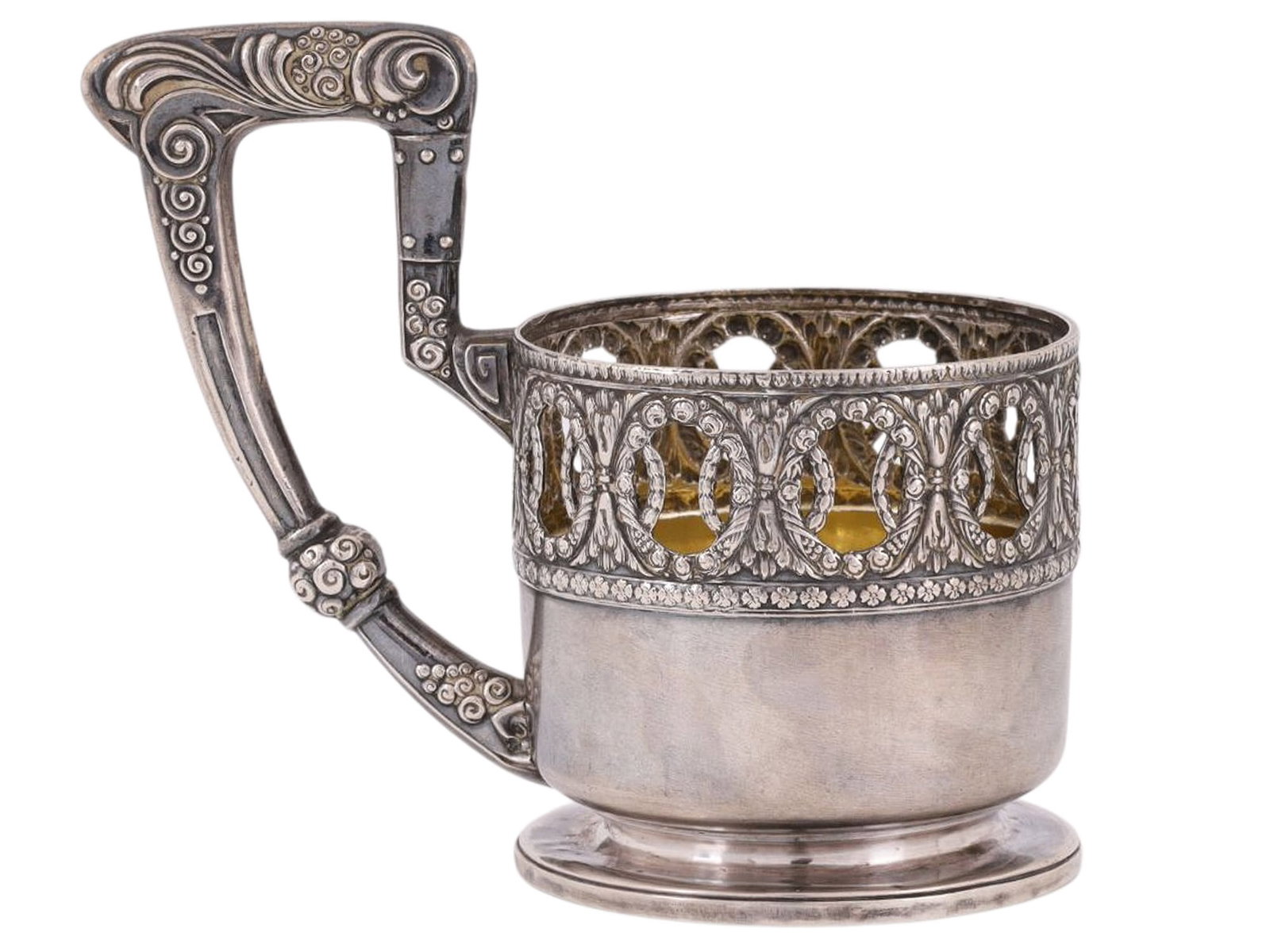 A RUSSIAN ART NOUVEAU SILVER TEA GLASS HOLDER, PRIVATE WORKSHOP, MOSCOW, LATE 19TH / EARLY 20TH: A cylindrical tea glass holder on a ring-shaped base, featuring a tall, curved handle with an intricate silhouette. The upper band is openwork, with a cut-out pattern of intertwining oval and stylized