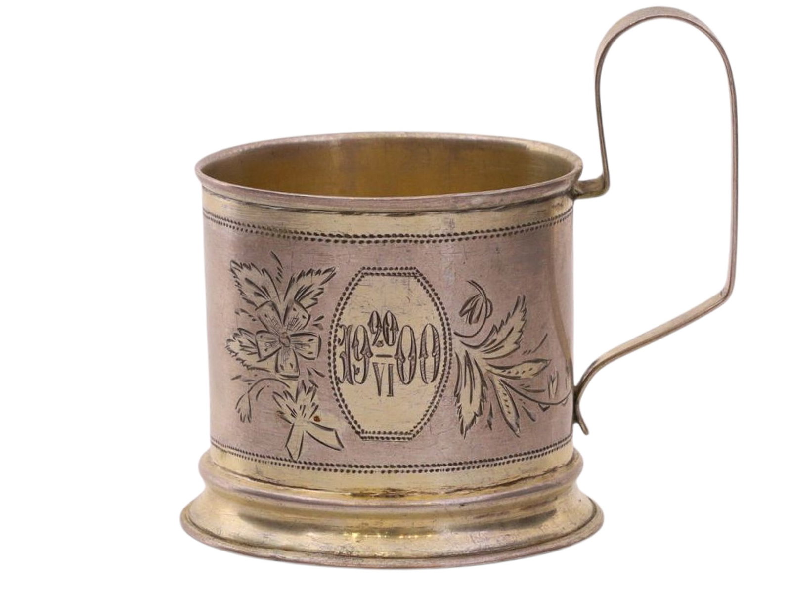 A RUSSIAN PARCEL-GILT SILVER TEA GLASS HOLDER, EARLY 20TH CEN.: A cylindrical tea glass holder with a rounded, flat handle, decorated on one side with a large medallion surrounded by an engraved asymmetrical floral motif. The date “19 20/VI 00” is engr