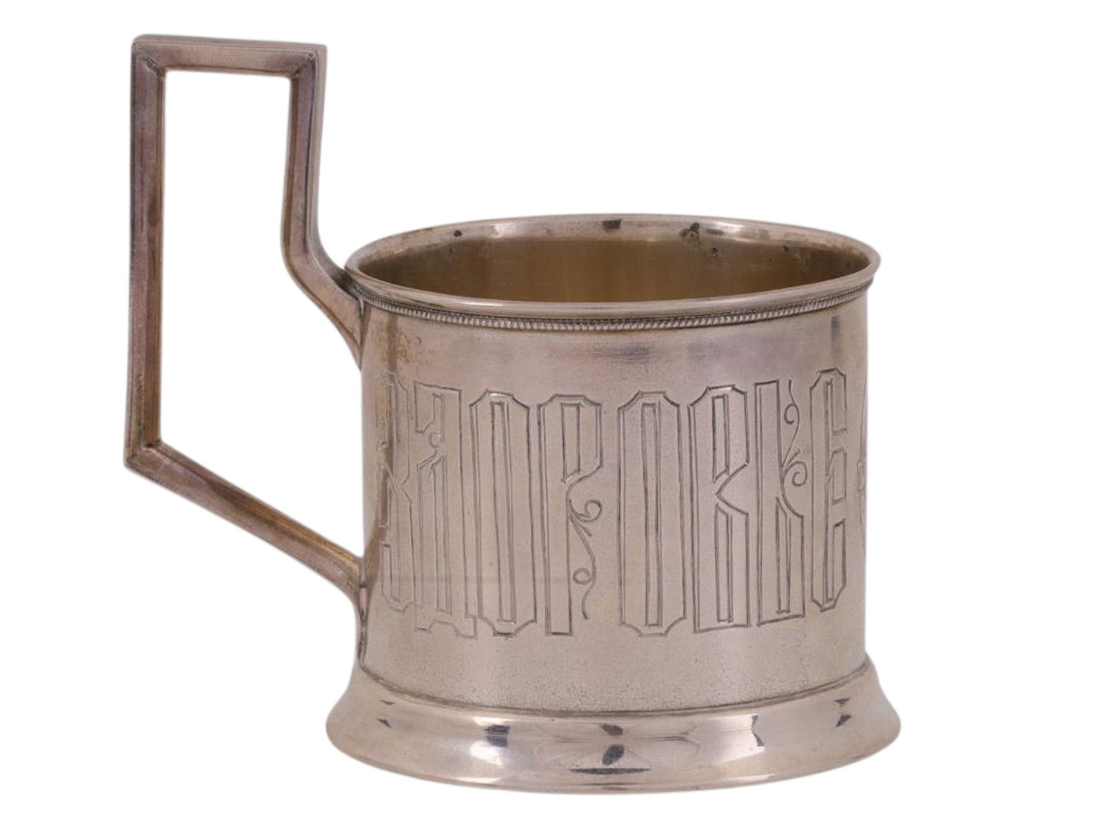 A RUSSIAN SILVER TEA GLASS HOLDER PRIVATE WORKSHOP, MOSCOW, EARLY 20TH CENTURY: Of cylindrical form with a rectangular handle. The body is centered with an engraved medallion in the form of a belt, enclosing a monogram beneath a crown. The surrounding inscription reads "DRINK TO 