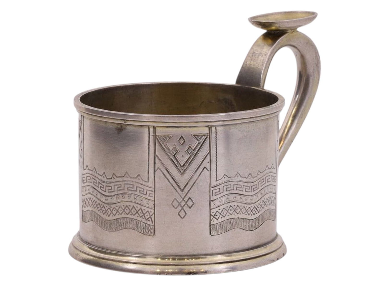 A RUSSIAN SILVER TEAGLASS HOLDER IN NEO-RUSSIAN STYLE, WORKSHOP OF ALEXANDER LYUBAVIN, 1878: A cylindrical tea glass holder with a rounded handle, decorated with a geometric pattern depicting Russian towels and folk lace. At the base of the handle and on the bottom are hallmarks: a two-headed