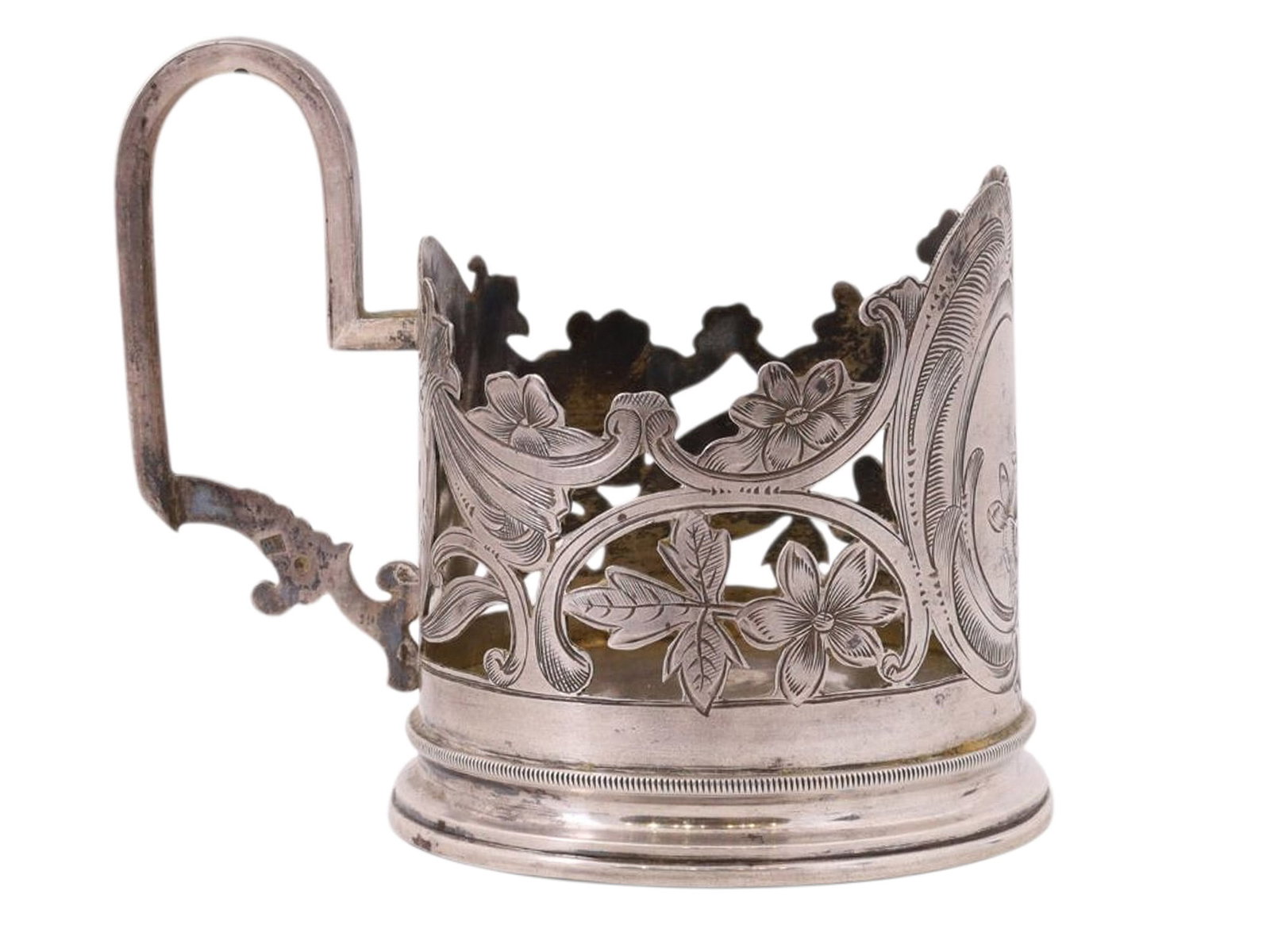 A RUSSIAN SILVER TEAGLASS HOLDER WITH OPENWORK FLORAL DESIGN, 19TH CENTURY: A cylindrical tea glass holder with a rocaille handle and a carved upper rim, decorated with a central ornamental cartouche and an openwork floral design. Silver, repoussé, engraving, and chasing