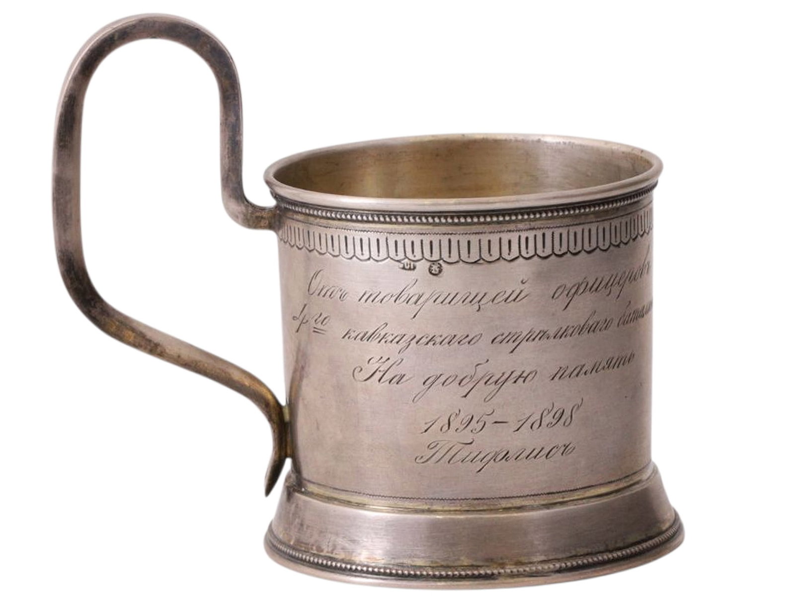 A RUSSIAN SILVER COMMEMORATIVE TEAGLASS HOLDER, UNKNOWN PRIVATE WORKSHOP, MOSCOW, 1890S: Of cylindrical form with an S shaped handle on a ring foot, the upper rim decorated with a geometric band. One side with a medallion in the Neo Russian style enclosing the inscription "To P.G. Felitsi