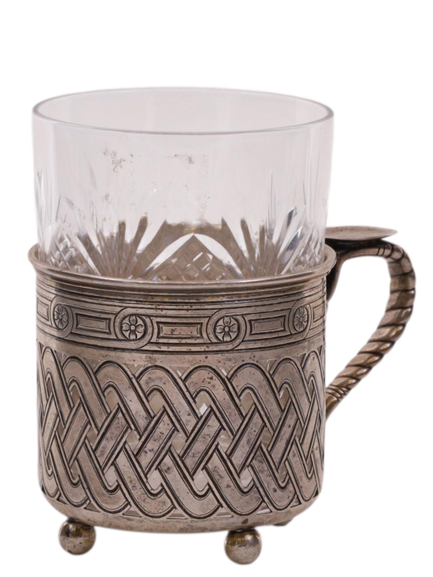 A RUSSIAN SILVER TEAGLASS HOLDER, MOSCOW, LATE 19TH CENTURY, BY OVCHINNIKOV: Of cylindrical form, in the Pan-Slavic style, raised on three balled feet and fitted with a twisted handle, the body richly decorated in the Pan-Slavic taste with interlacing strapwork in a continuous