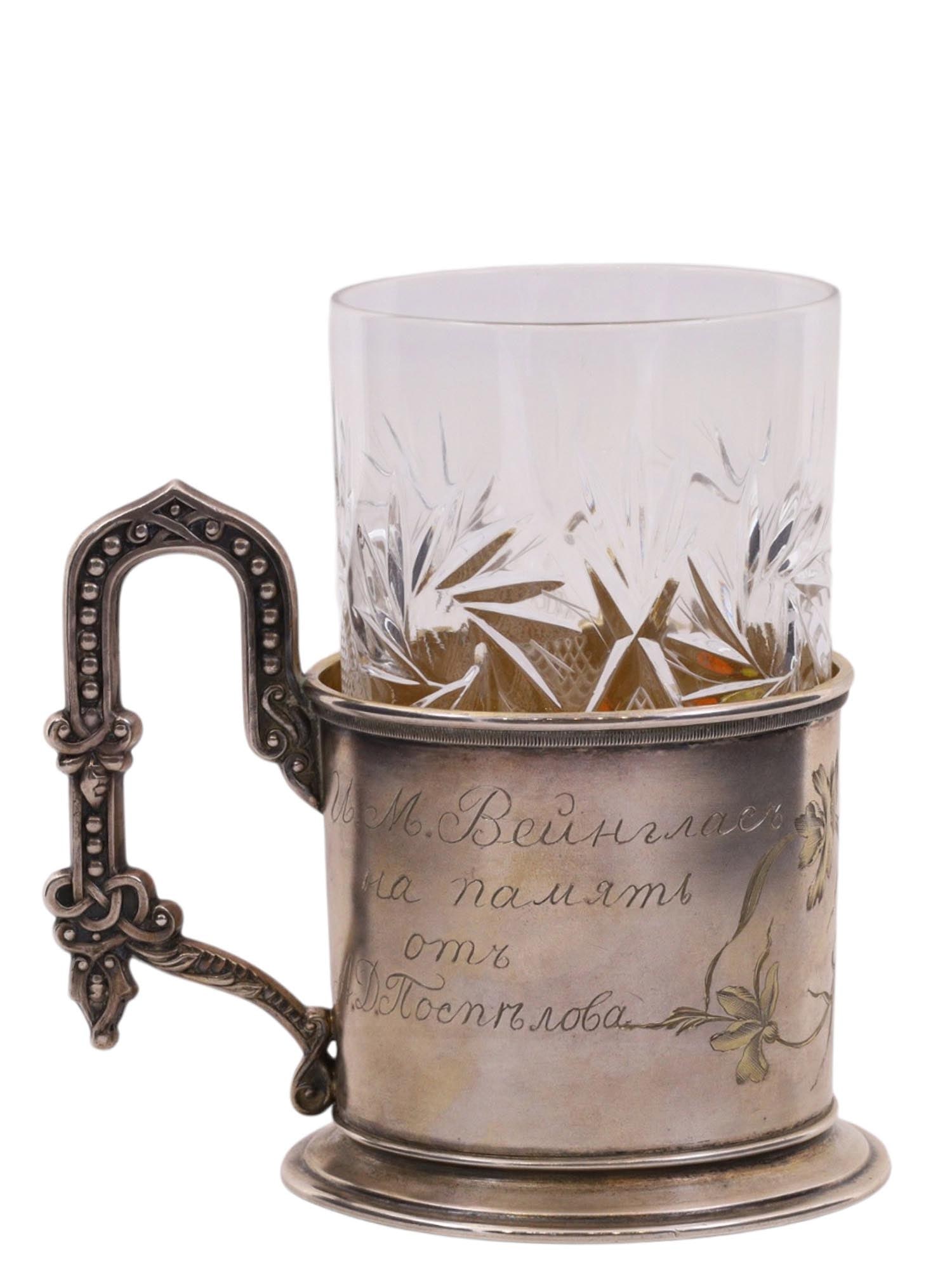 A RUSSIAN PARCEL-GILT SILVER TEA GLASS HOLDER WITH A CUT-CRYSTAL GLASS: Of cylindrical form on a ring foot, with a relief twisted handle. The body is decorated with a naturalistic floral composition of flowers and butterflies in the Art Nouveau style. One side bears a pre