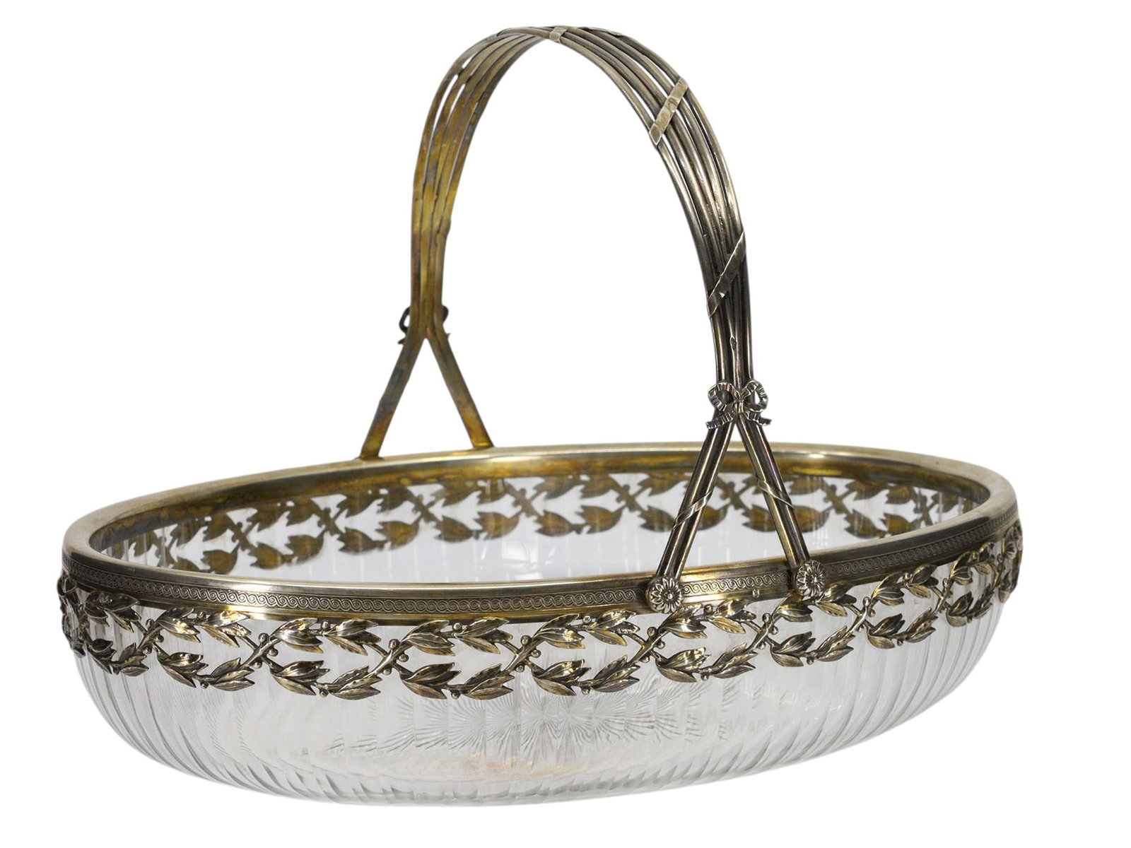 A SILVER-MOUNTED CRYSTAL FRUIT BOWL, FRANCE, CA. 1890: The oval crystal body is finely cut with vertical fluting and a star-cut base, mounted with a pierced silver gilt rim of intertwined laurel leaves symbolizing victory and honor. The swing handle is fo