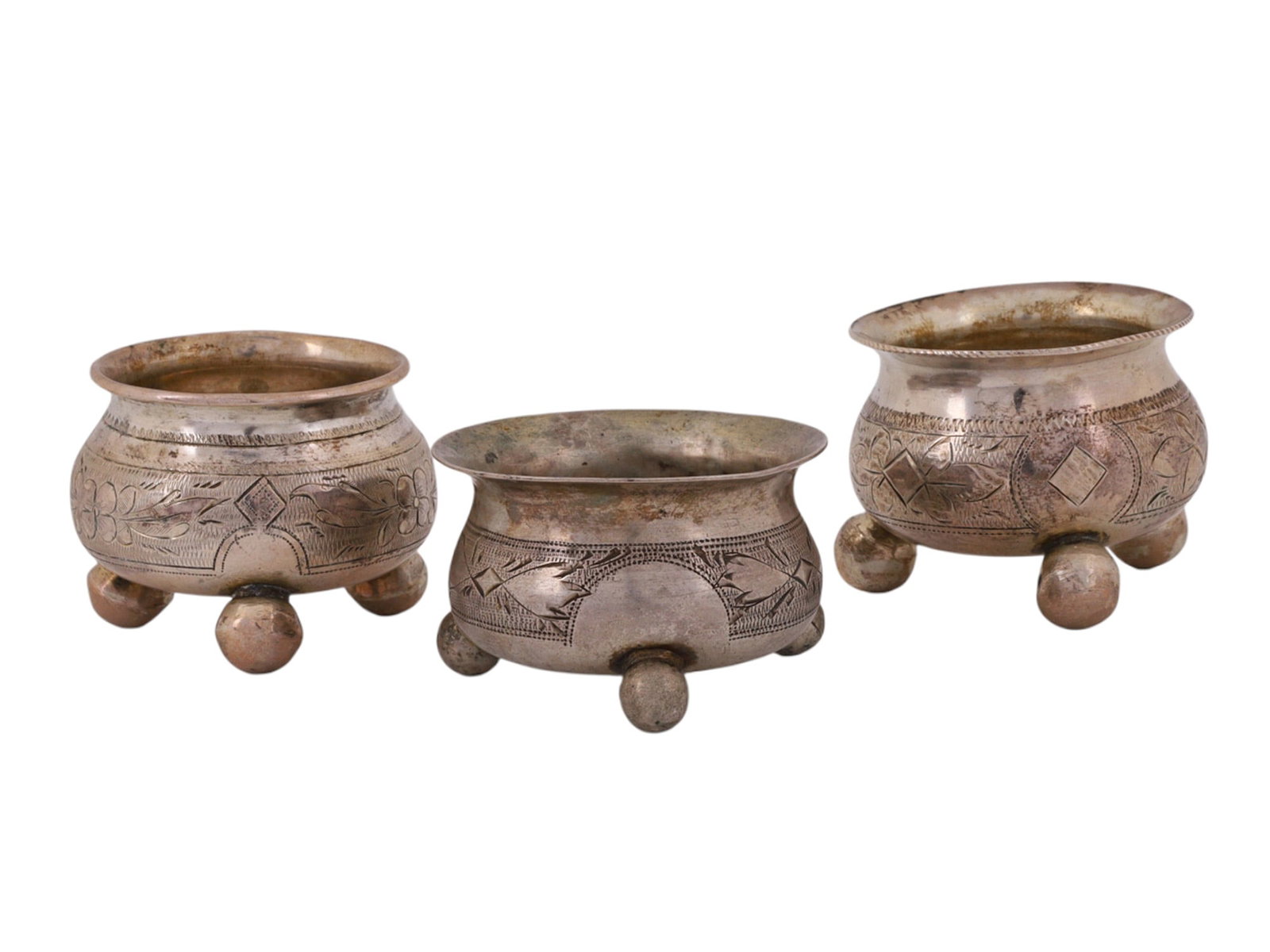 A LOT OF THREE RUSSIAN SILVER SALT CELLARS, MOSCOW, 1886: Comprising three salt cellars of rounded form, each raised on three ball feet with slightly flared rims. The bodies are decorated with engraved geometric and stylized foliate ornament forming continuo