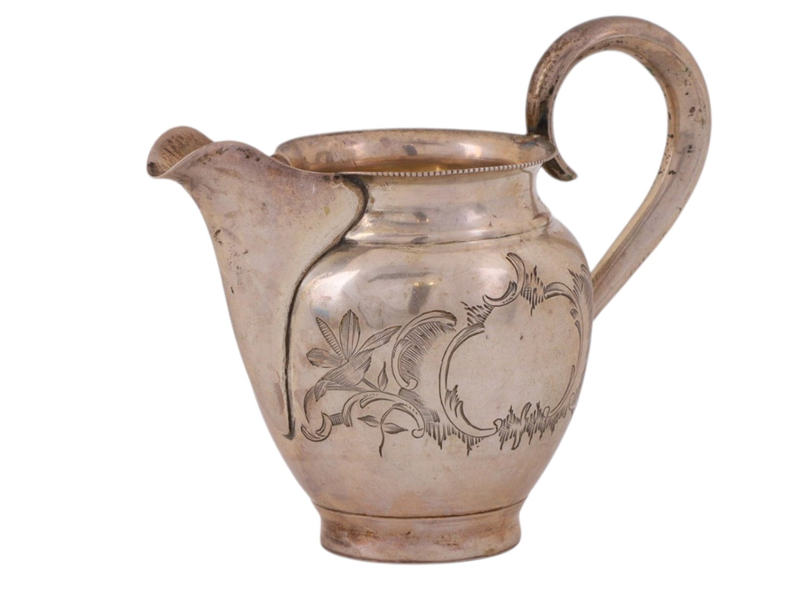 RUSSIAN PARCEL GILT SILVER CREAMER, MOSCOW, LATE 19TH CENTURY: Of rounded baluster form on a short circular foot, with a flaring rim, pronounced spout, and a high looping handle. The body is engraved with a shaped cartouche framed by scrolling foliate ornament, w