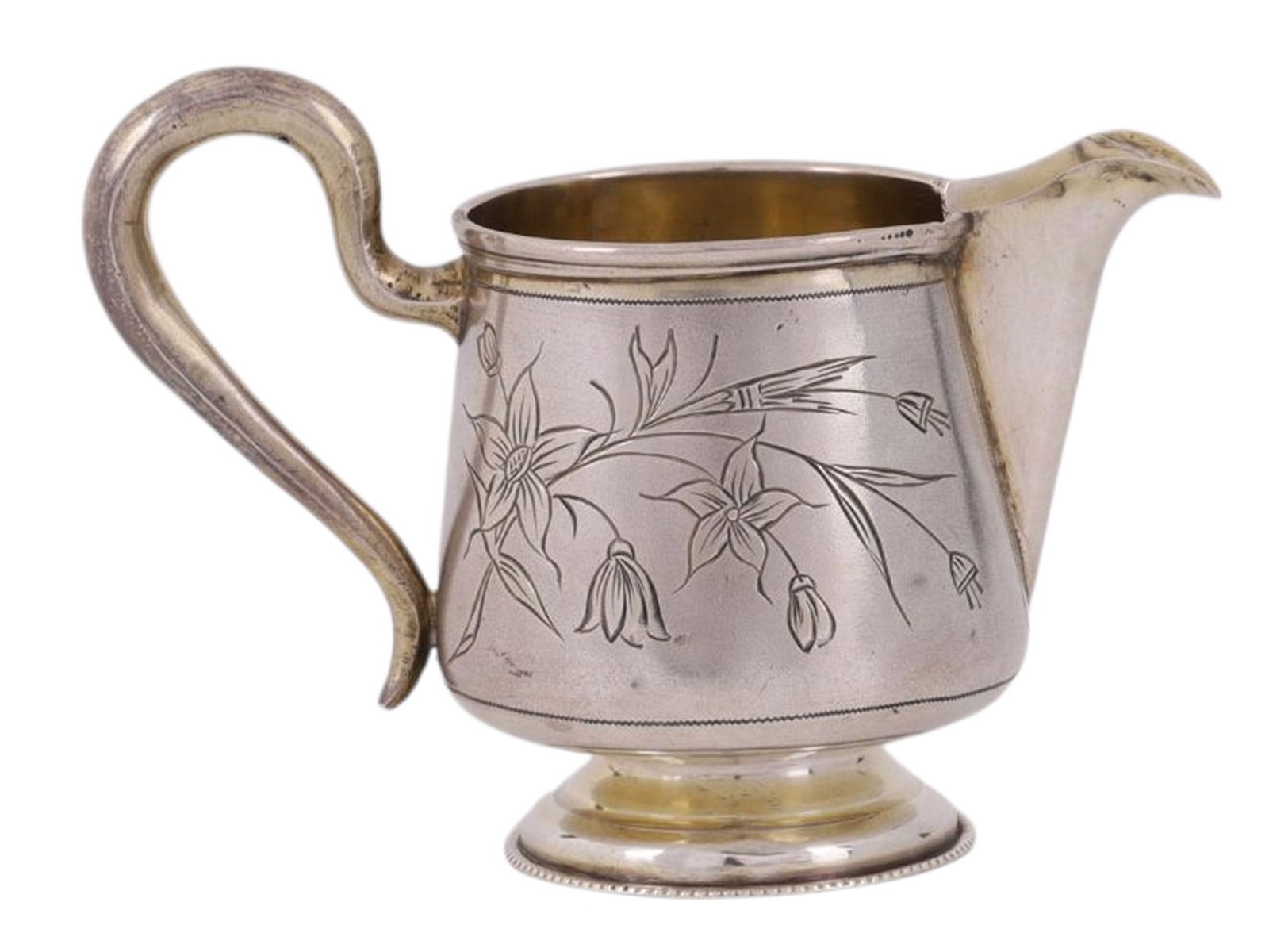 A RUSSIAN PARCEL-GILT SILVER CREAMER WITH ENGRAVED DECORATION: A Russian parcel-gilt silver creamer with engraved floral decoration to each side, a curved handle affixed to the back, and a sloped spout emanating from the front.Hallmarks: Cyrillic 'MG' maker's mar