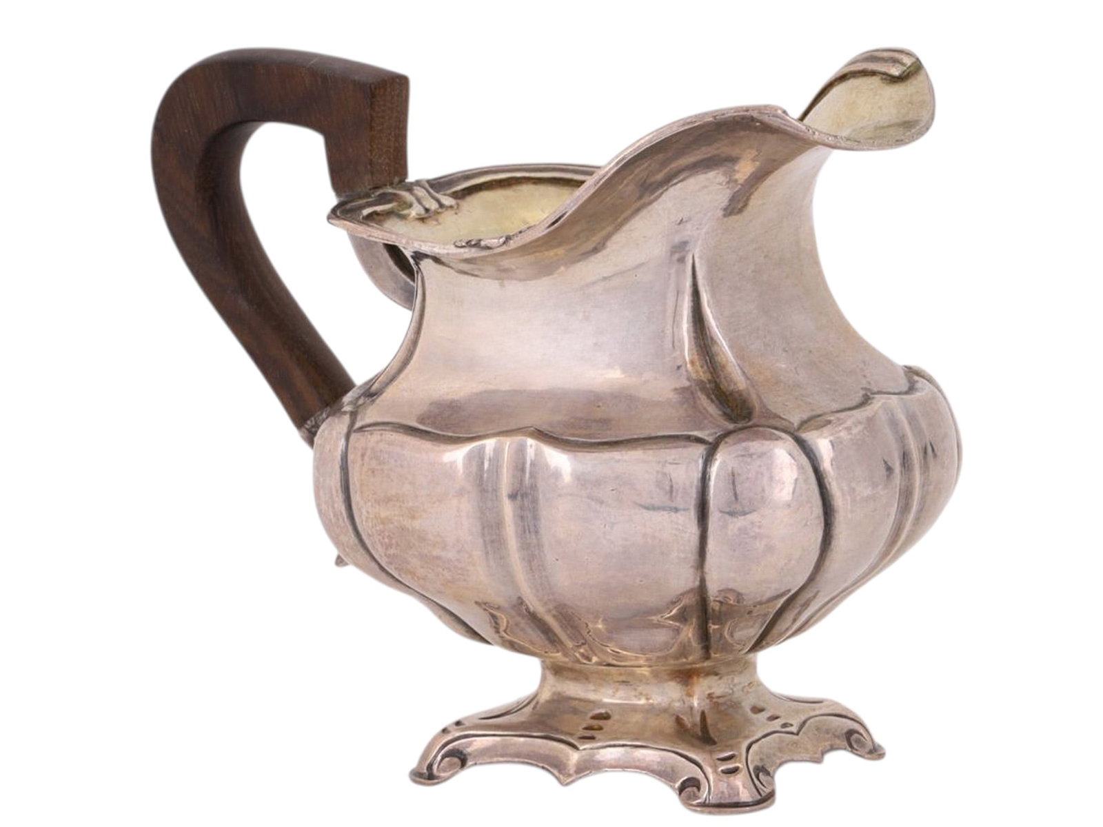 A MID-19TH CENTURY RUSSIAN SILVER CREAMER WITH WOOD HANDLE: A Russian silver creamer produced in 1848, affixed with a curved wooden handle, its belly of a generally squared form with rounded lobes protruding. Sat atop a molded foot via a slender stem.Hallmarks